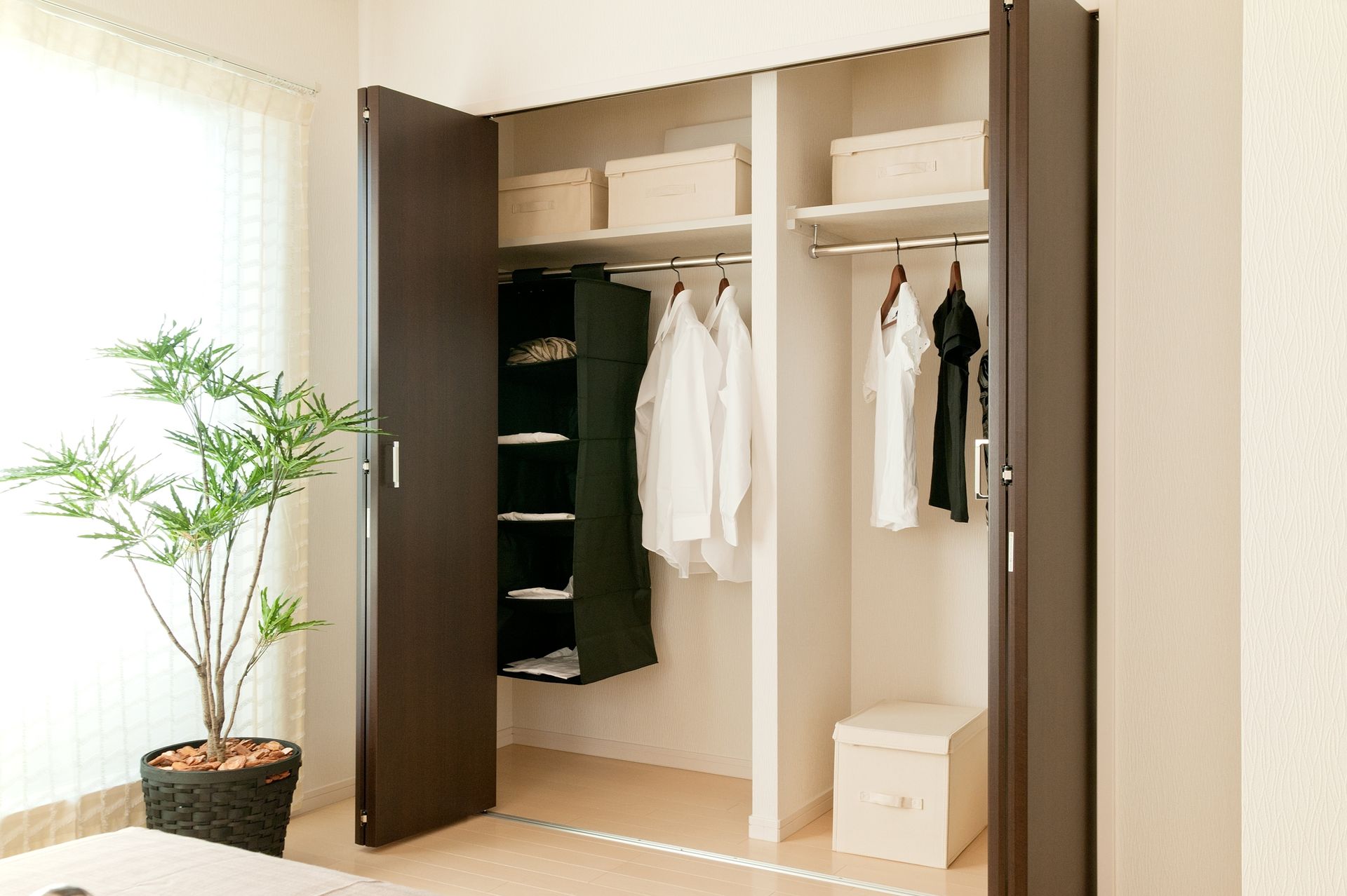 Open closet with hanging clothes, shelves, and storage boxes in a bright room