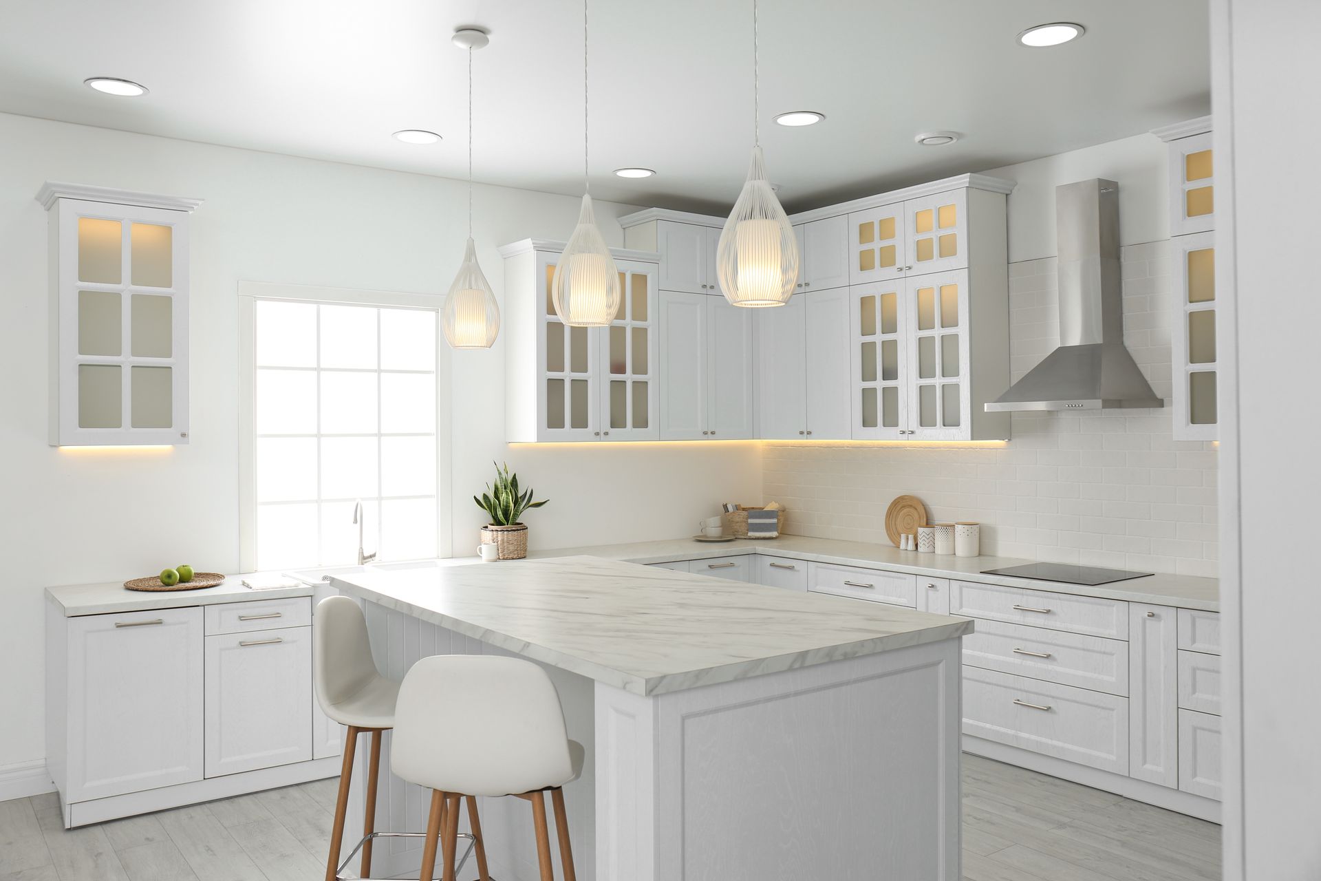 Bright white modern kitchen with marble island, pendant lights, and stainless-steel range hood