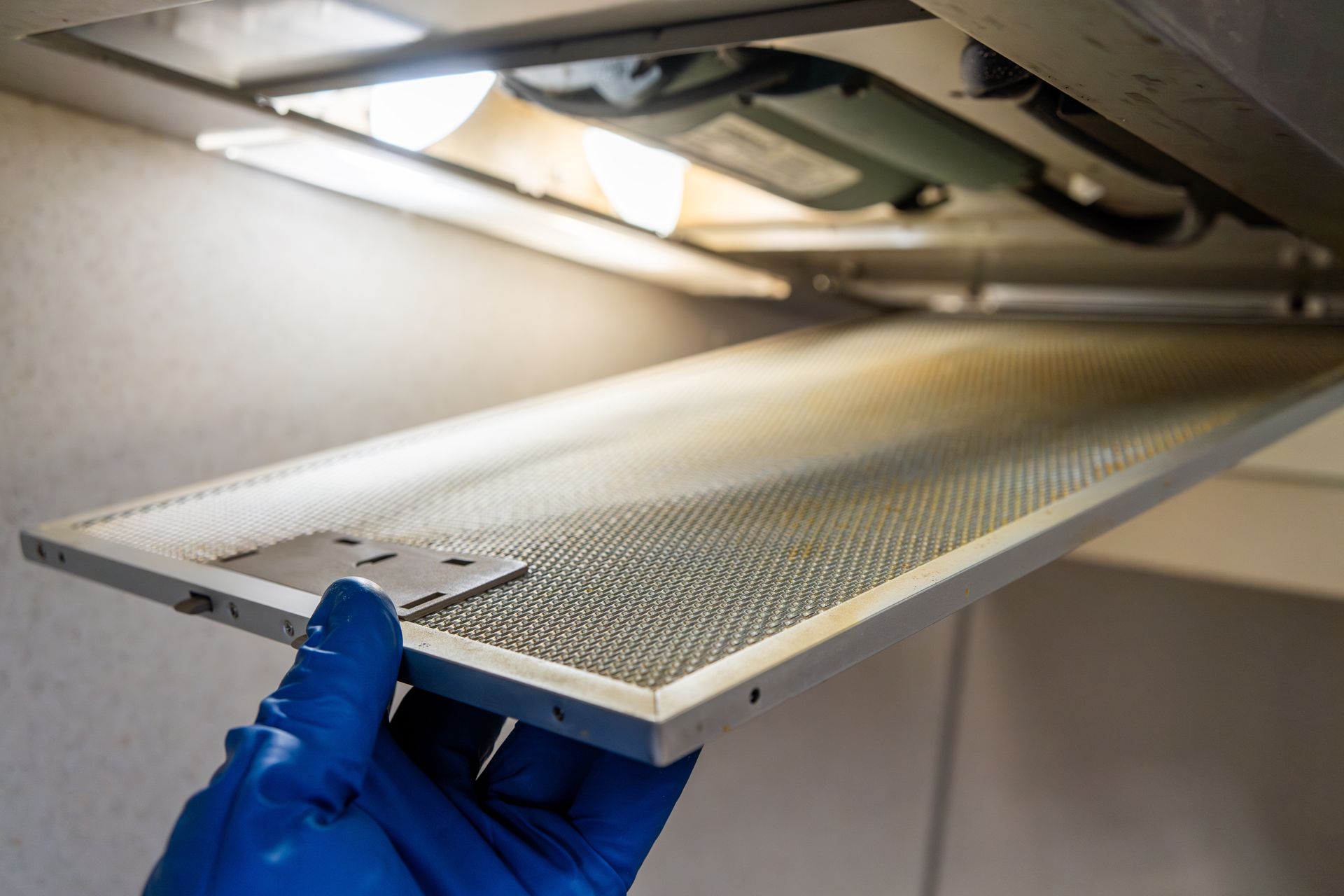 Gloved hand removing a metal air filter from a ceiling vent under bright light