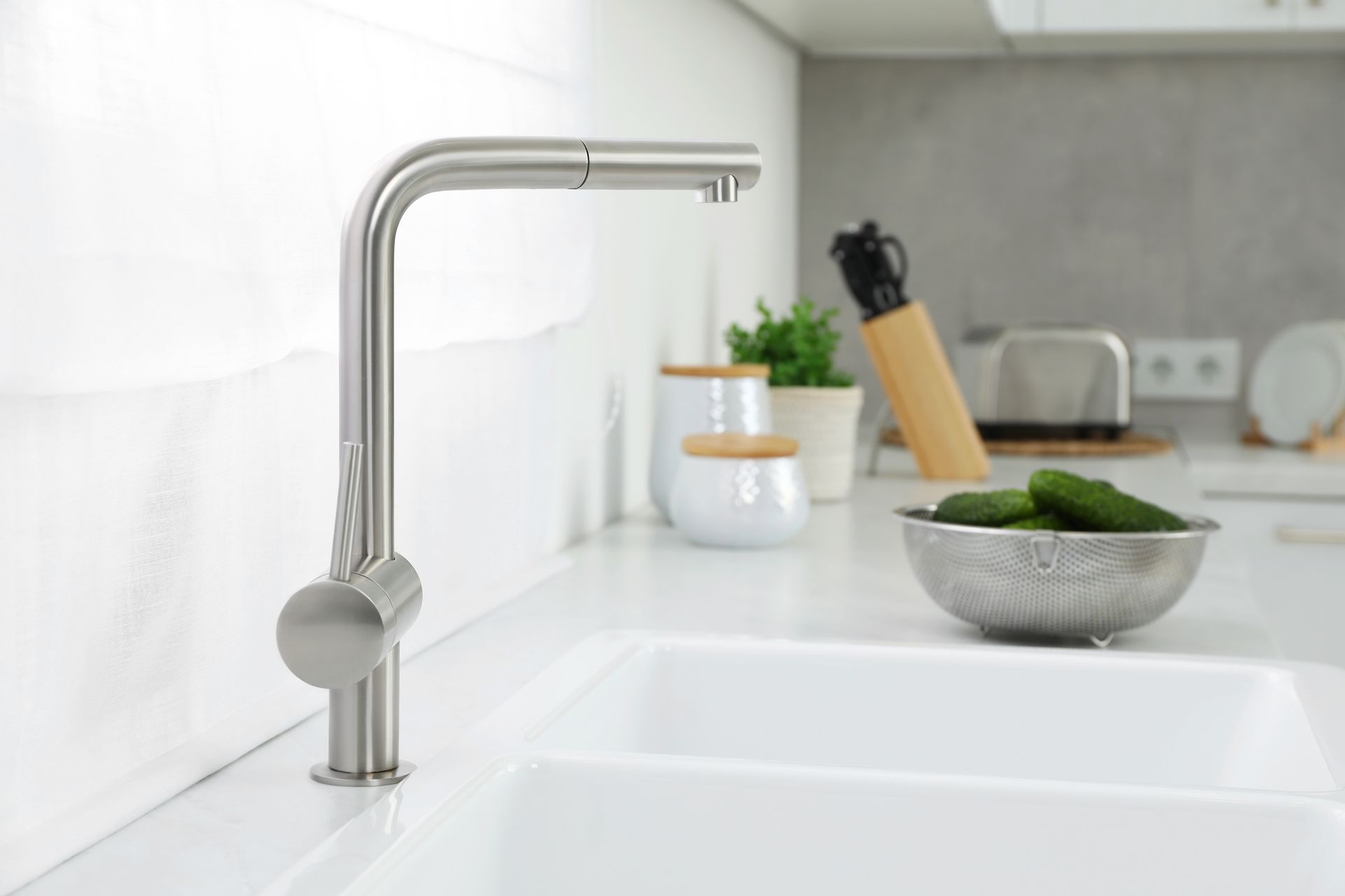 Modern kitchen sink with stainless faucet, bowl of greens, and utensils in the background