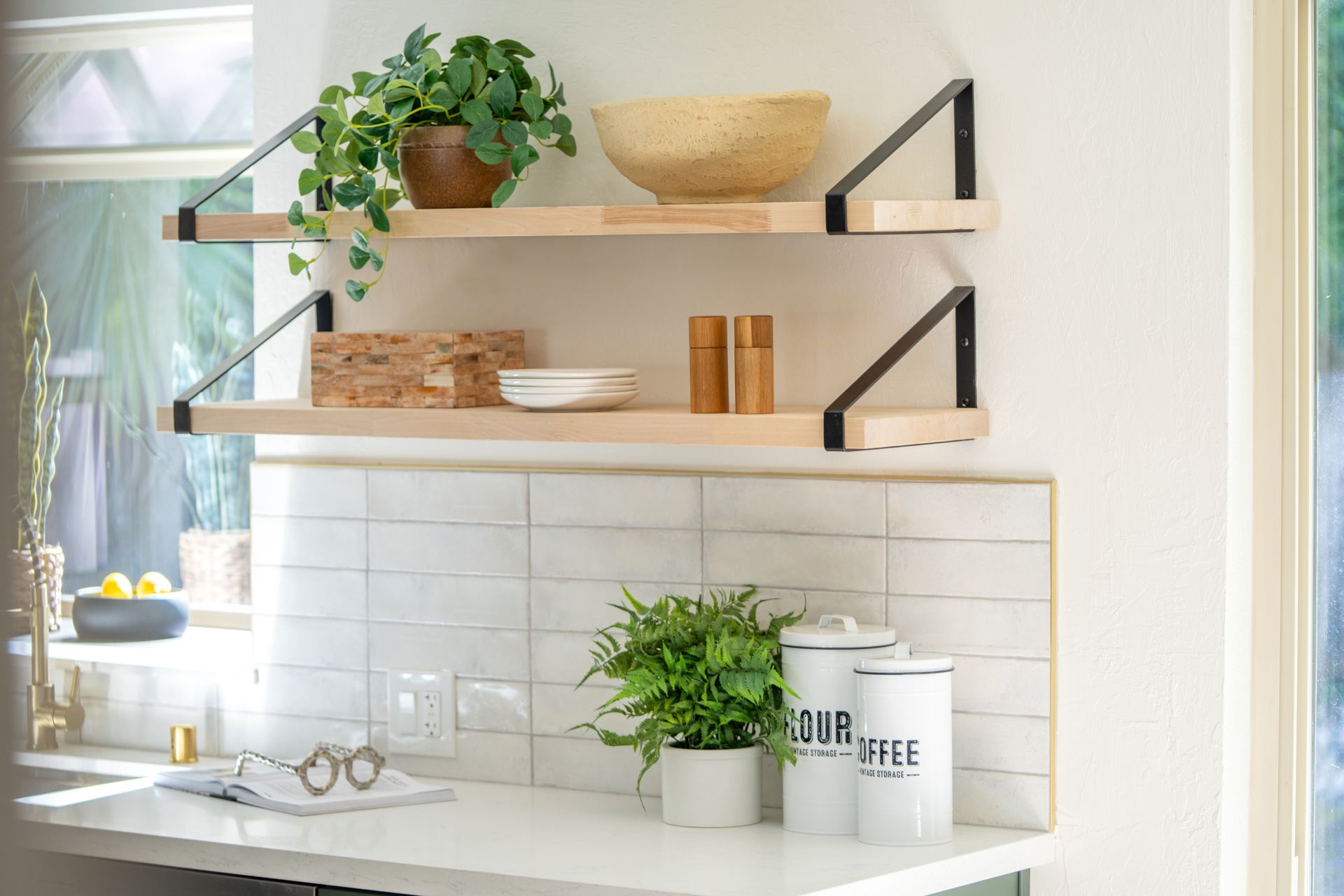 Floating shelves with plants, bowls, and dishes above a white kitchen counter and backsplash