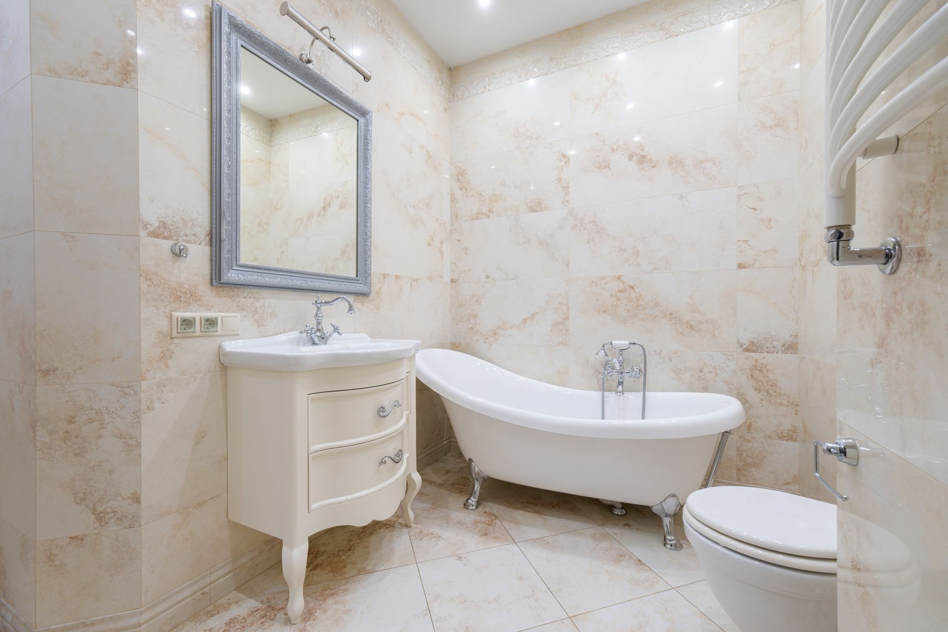 Elegant marble-tiled bathroom with a freestanding tub, vanity, mirror, and toilet