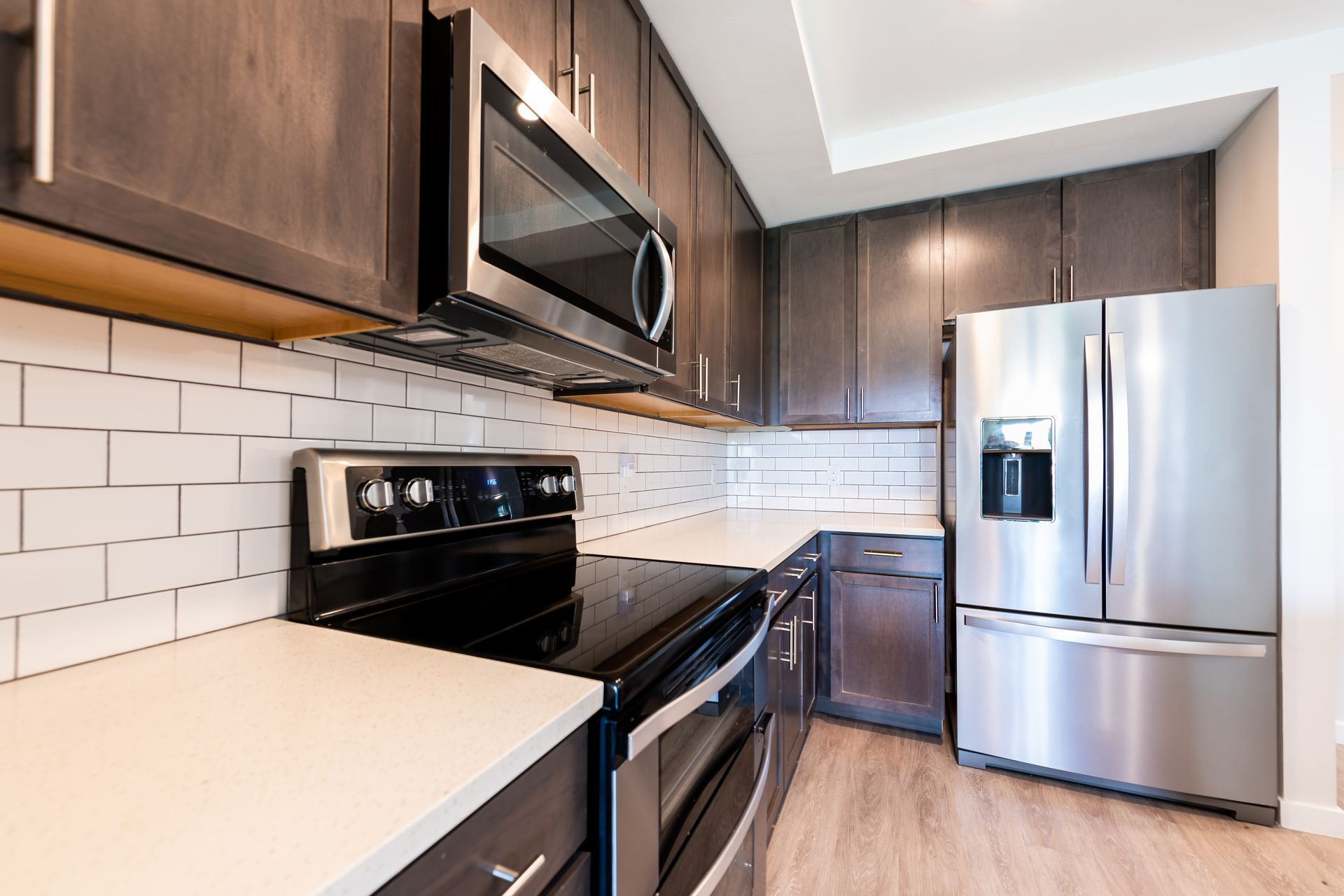 Modern kitchen with stainless steel appliances, dark cabinets, white tile backsplash, and light countertops