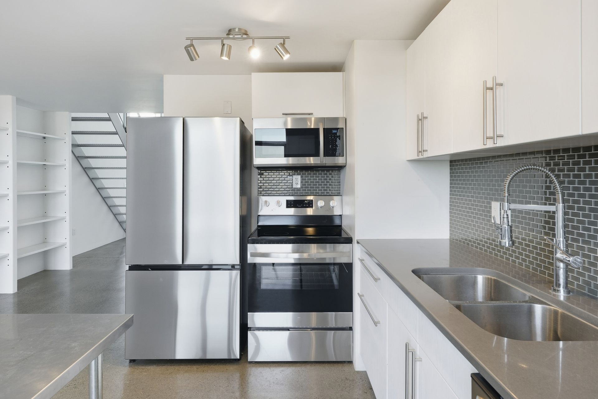 Modern white kitchen with stainless steel appliances, gray countertops, and mosaic tile backsplash