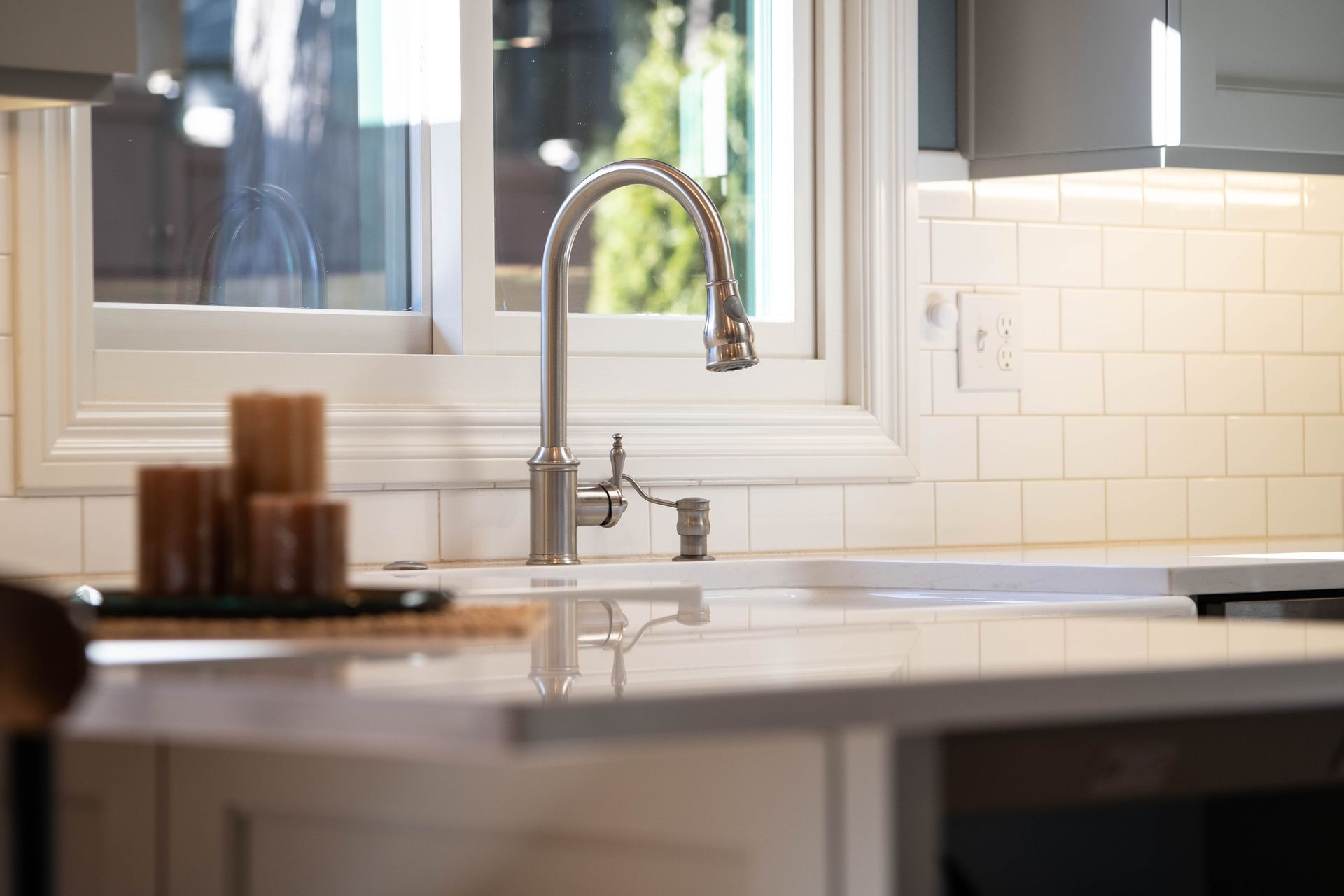 Bright kitchen sink with chrome faucet beside a white tile backsplash and window.