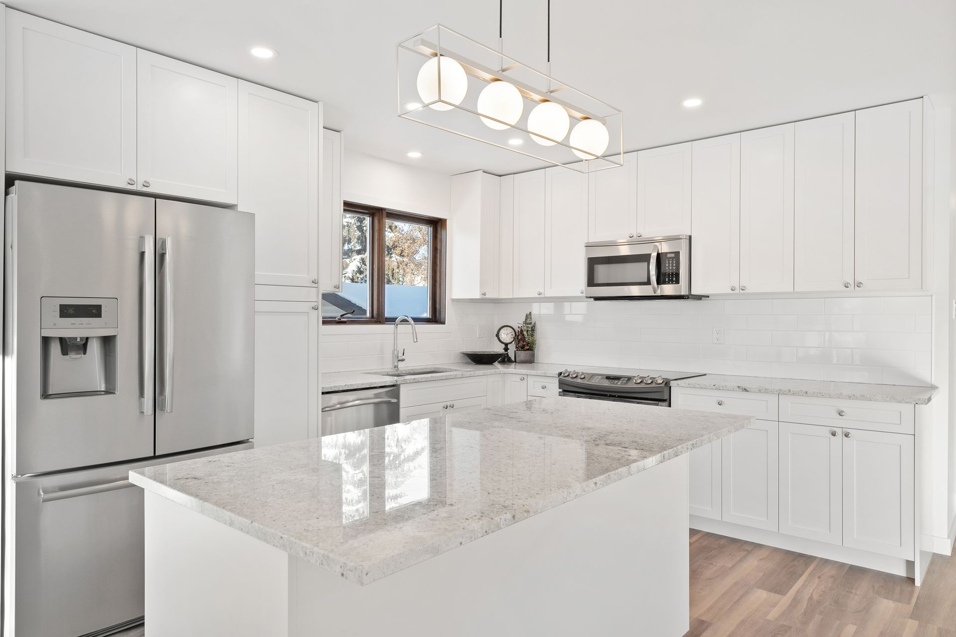 Bright modern white kitchen with stainless steel appliances, marble island, and pendant lights