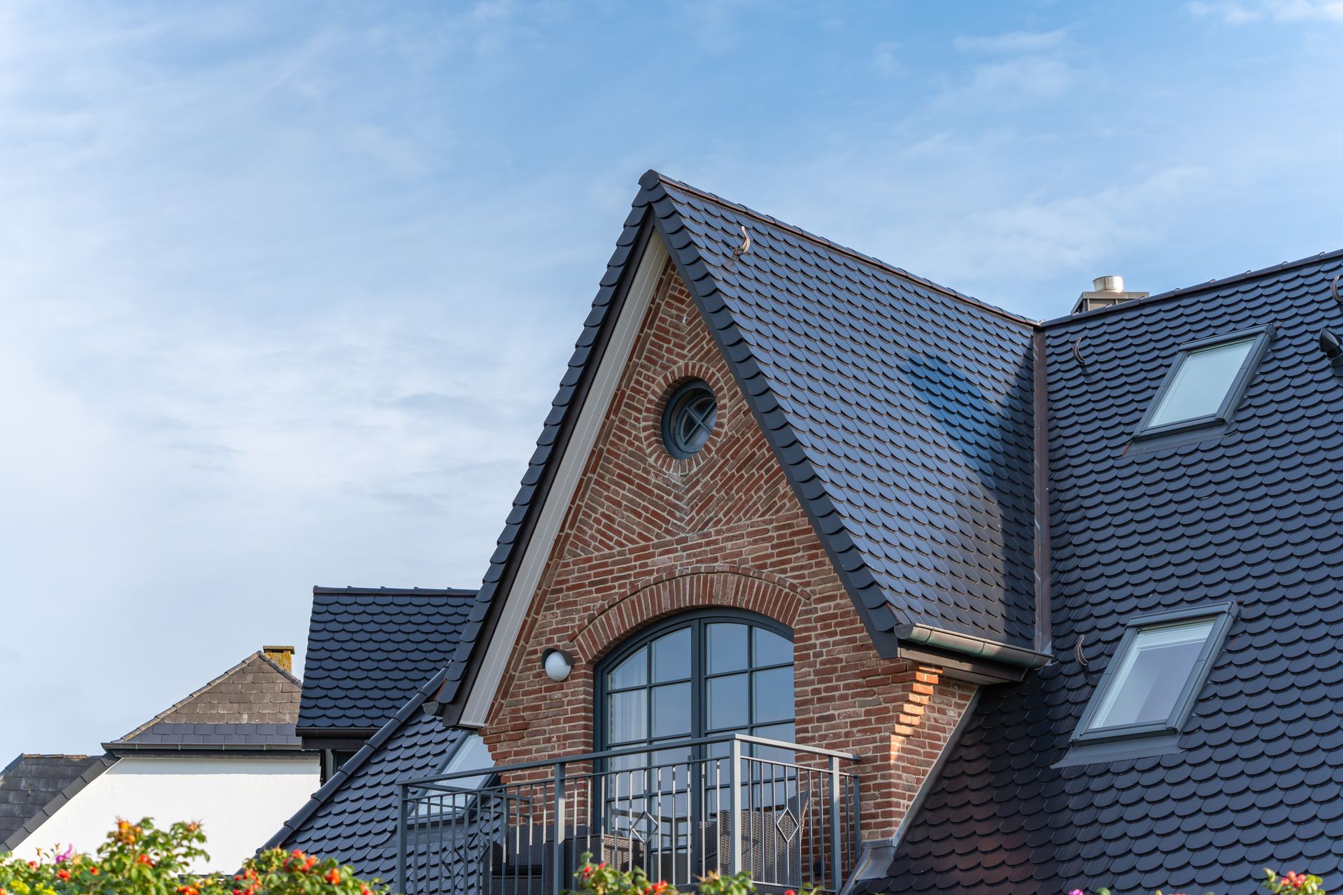 Brick house with steep dark roof, arched window, and skylight under a blue sky