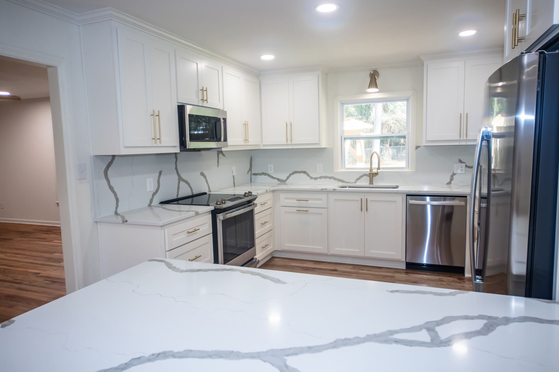 Bright white kitchen with marble island, stainless steel appliances, and white cabinets