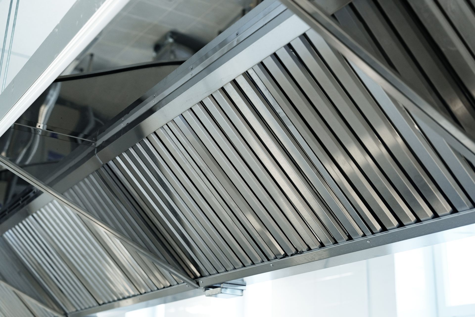 Stainless steel kitchen range hood with slatted vents and filters under a cabinet