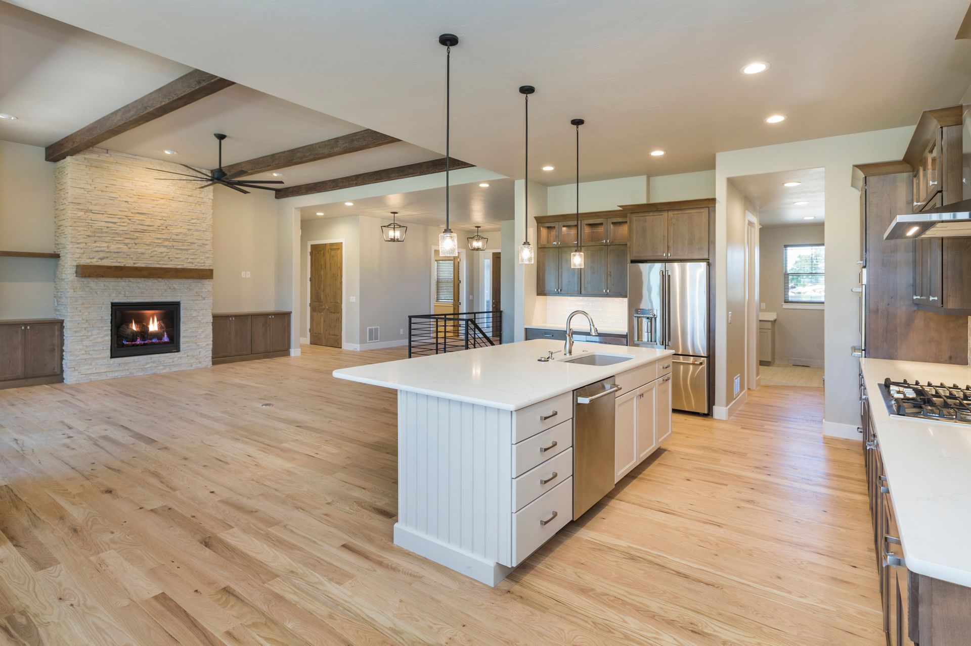 Bright open kitchen and living area with white island, wood floors, exposed beams, and fireplace