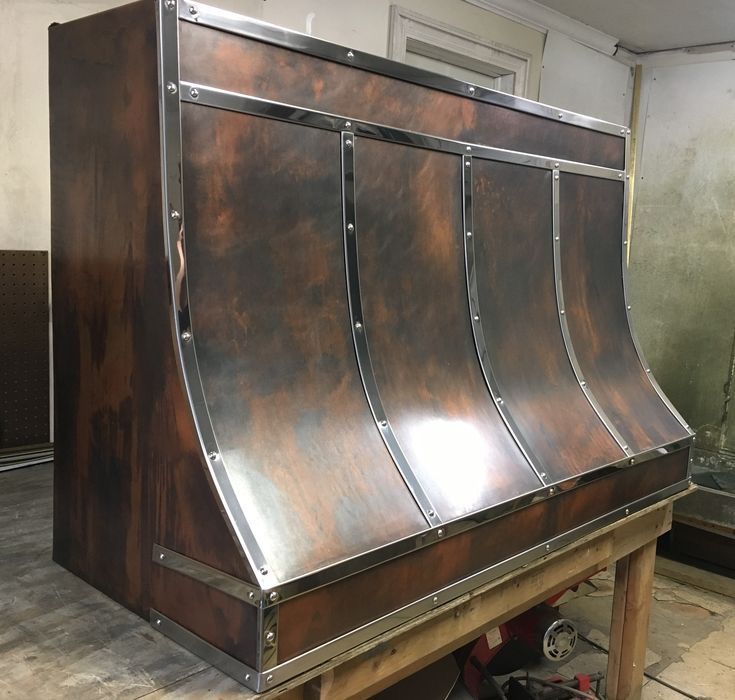 Copper-toned metal hood with curved panels on a workbench in a workshop