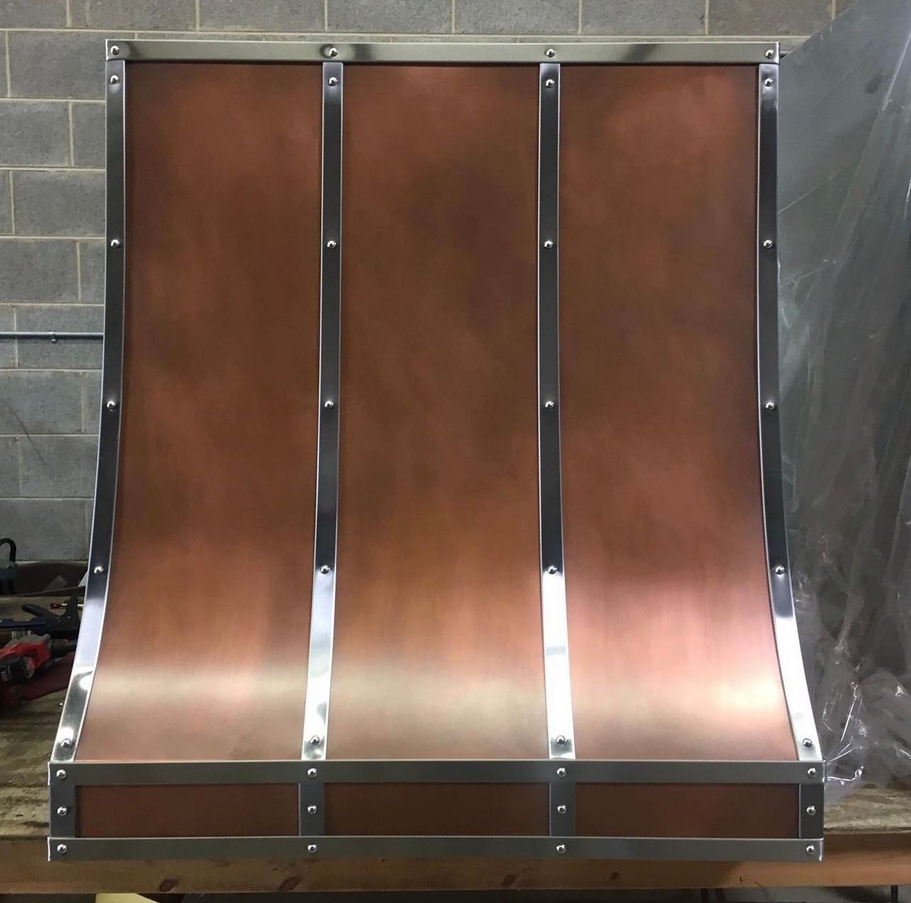 Three-panel copper-colored chute or slide mounted in a metal frame against a concrete wall