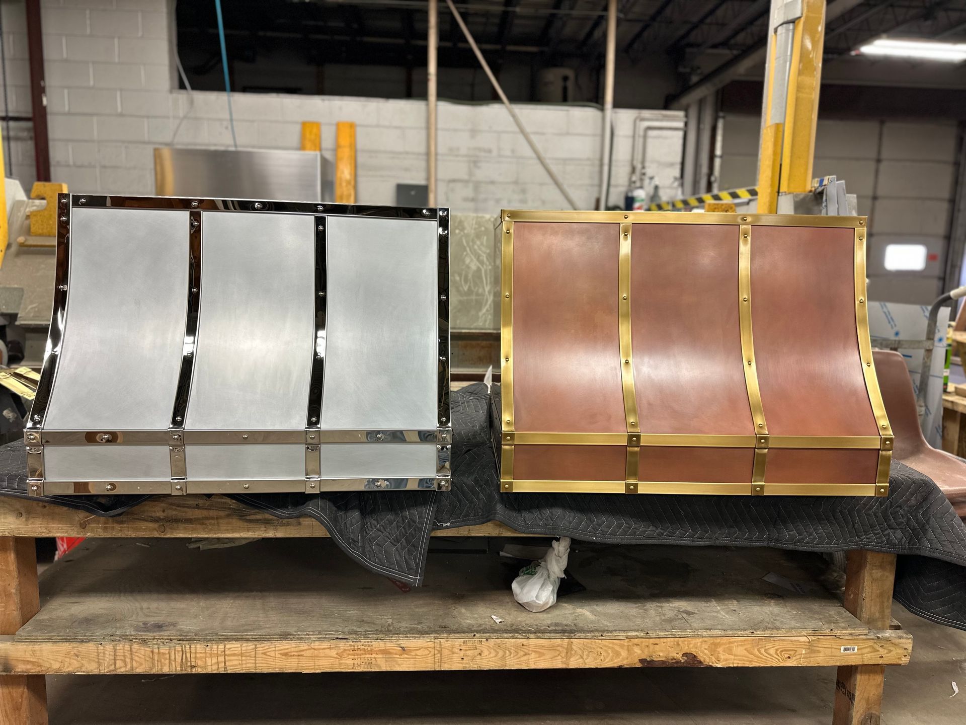 Two metal duct panels, one silver and one copper, on a wooden pallet in a warehouse