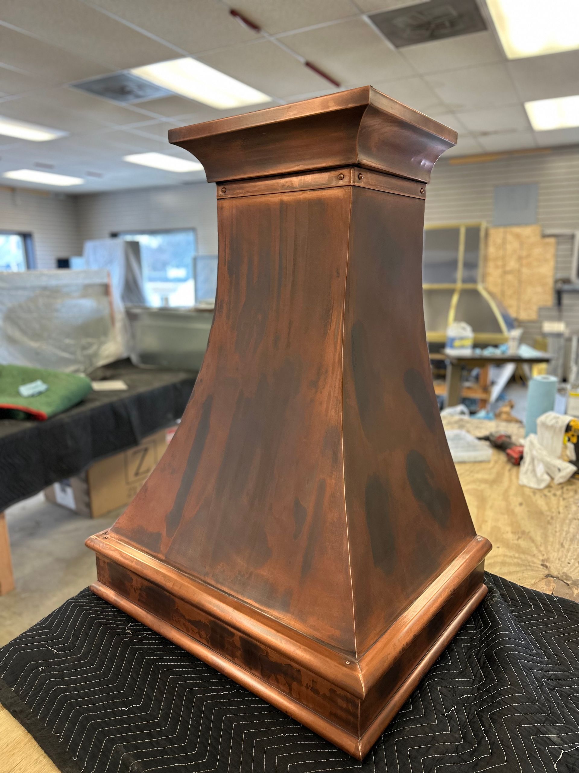 Copper-colored metal pedestal or decorative base on a black mat in a workshop.