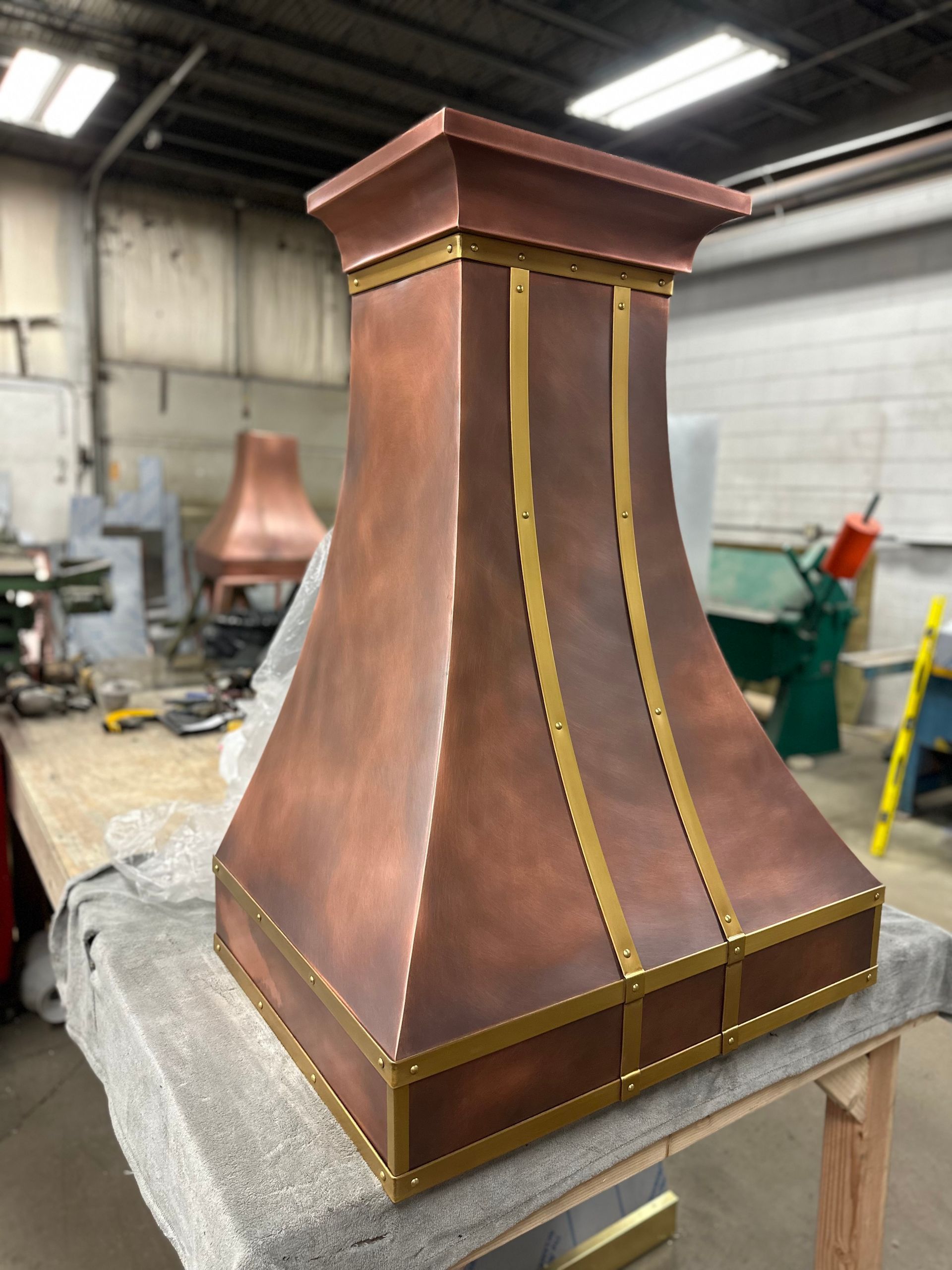 Copper-colored decorative metal hood with gold trim on a workshop table