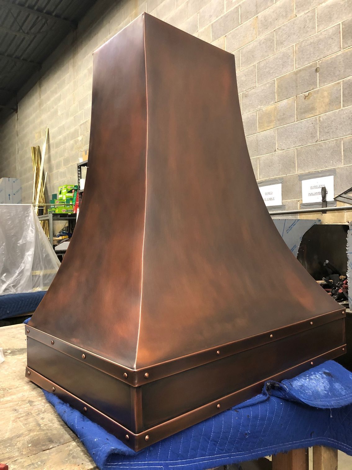 Copper-colored metal range hood in a workshop, sitting on a blue moving blanket.