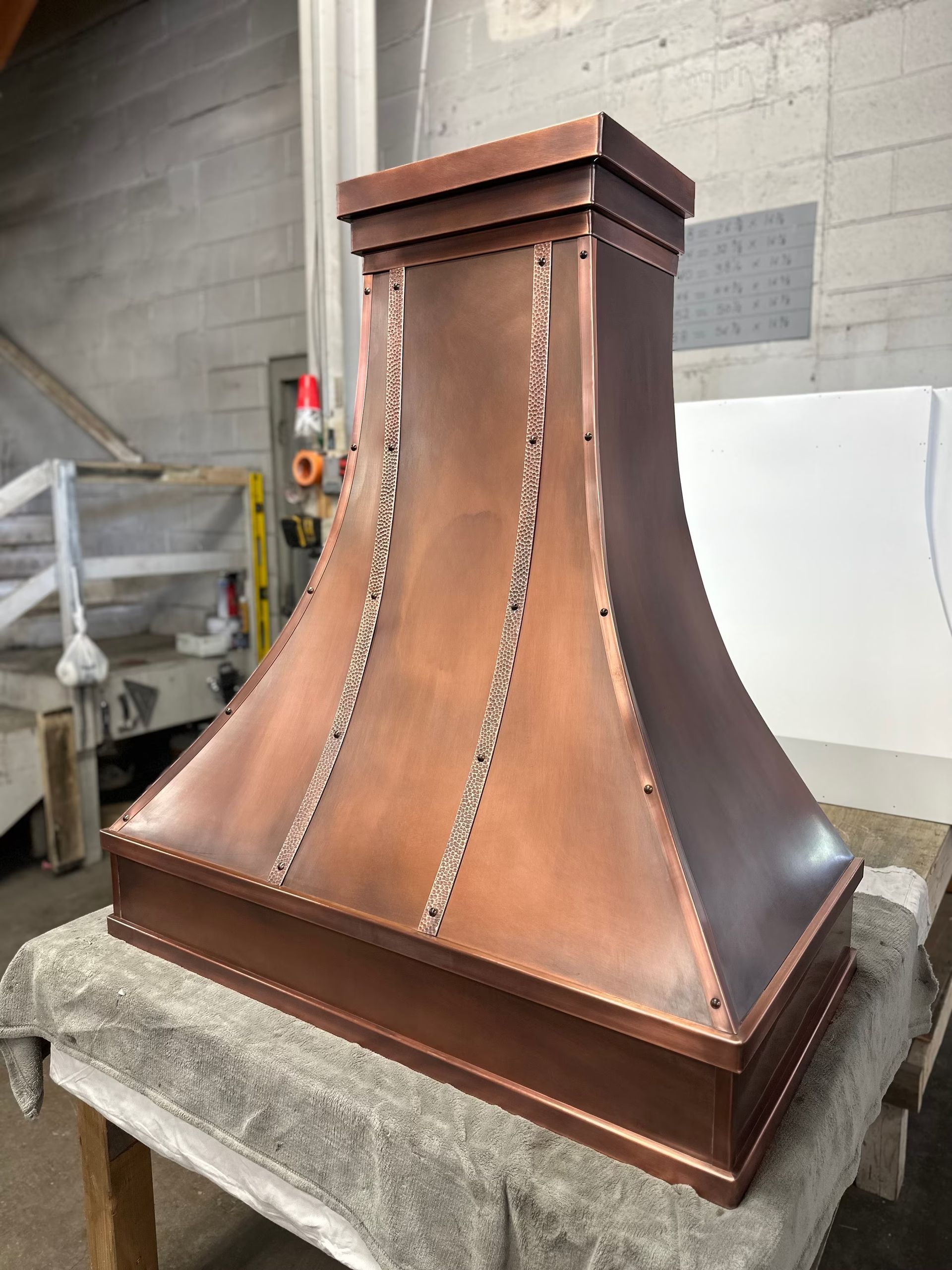 Copper range hood with riveted seams, sitting in a workshop on a workbench