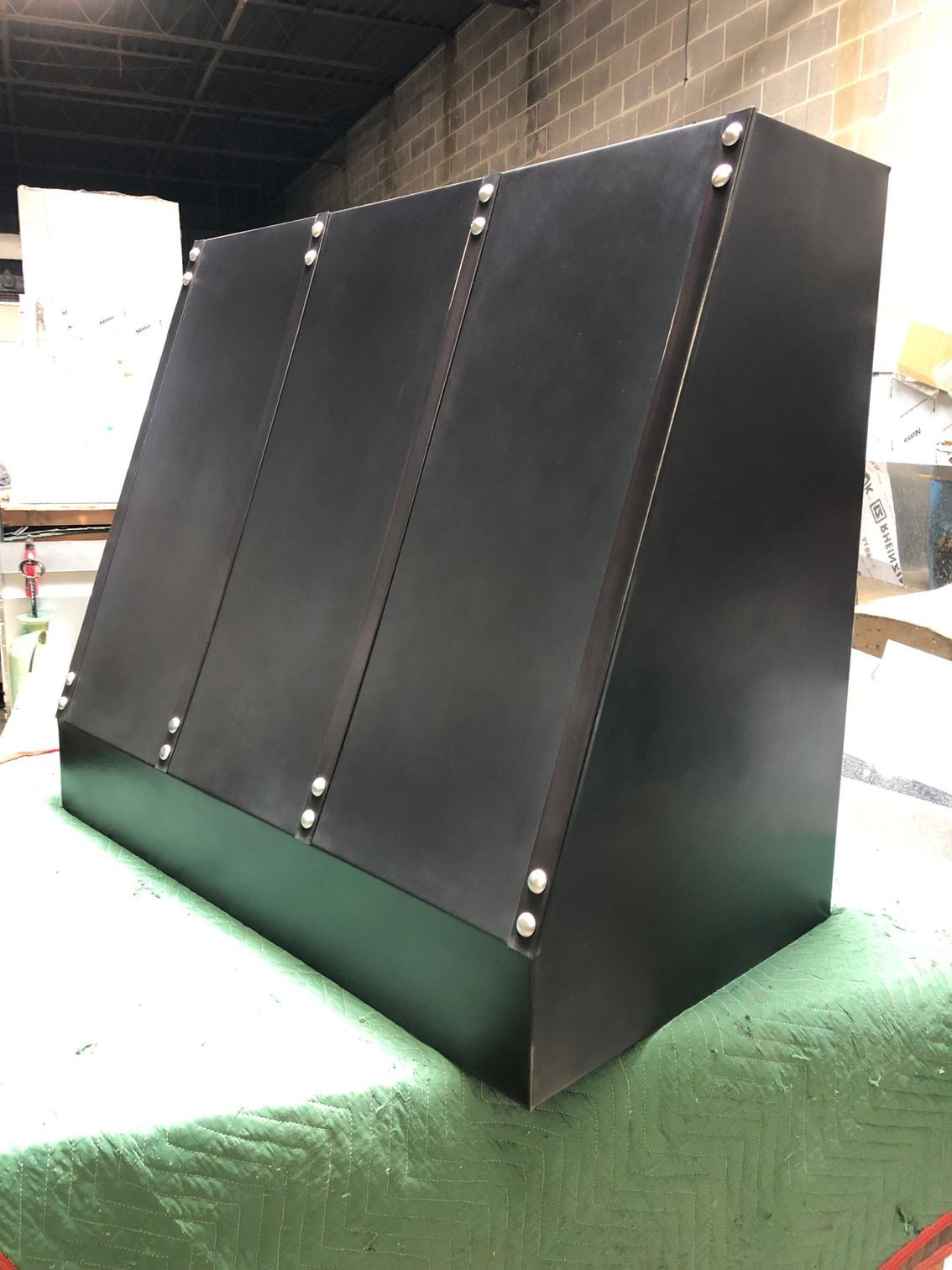 Black angled panel with rivets on a green table in an indoor workshop