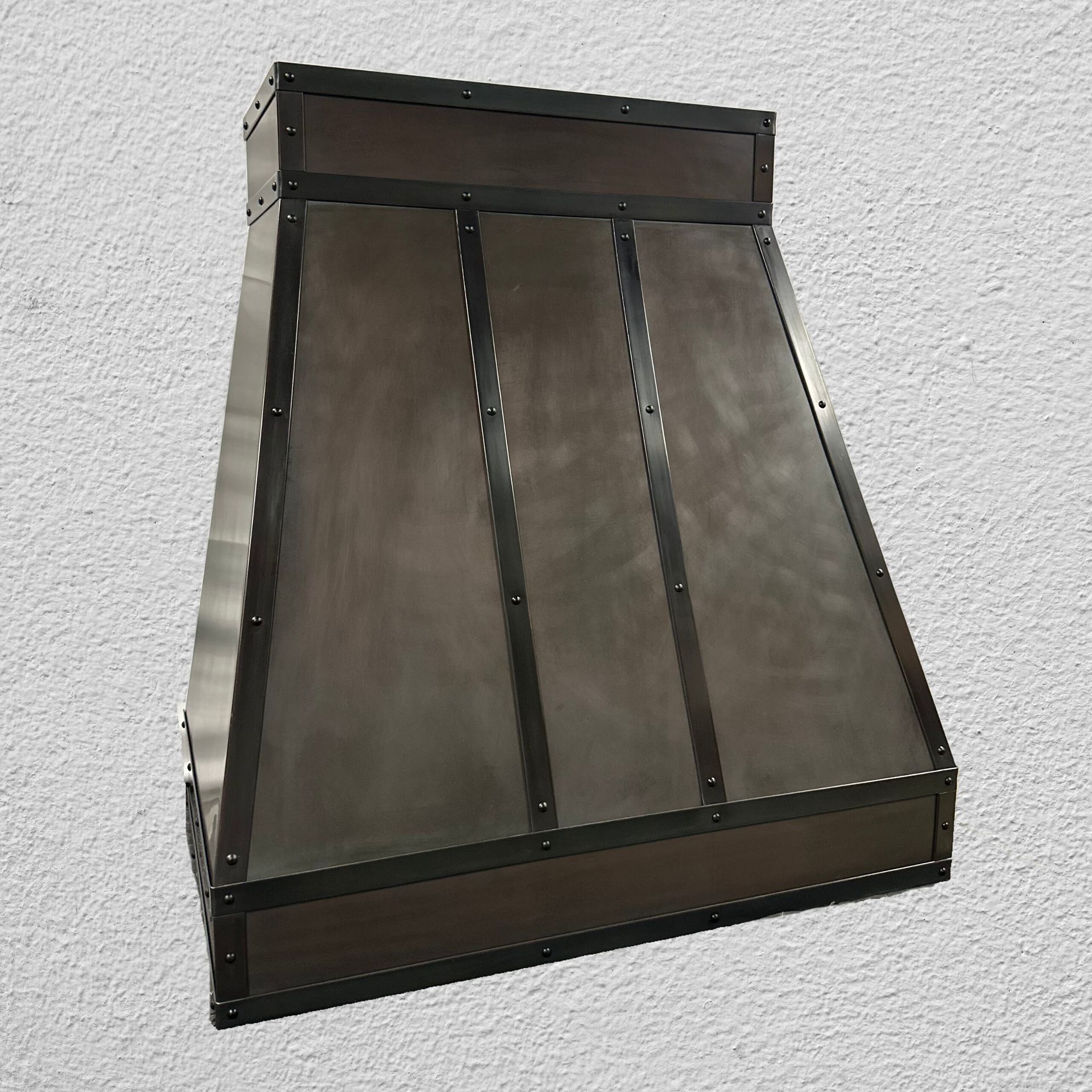 Dark metal wall-mounted funnel or hood with angled panels and black trim against a white textured wall