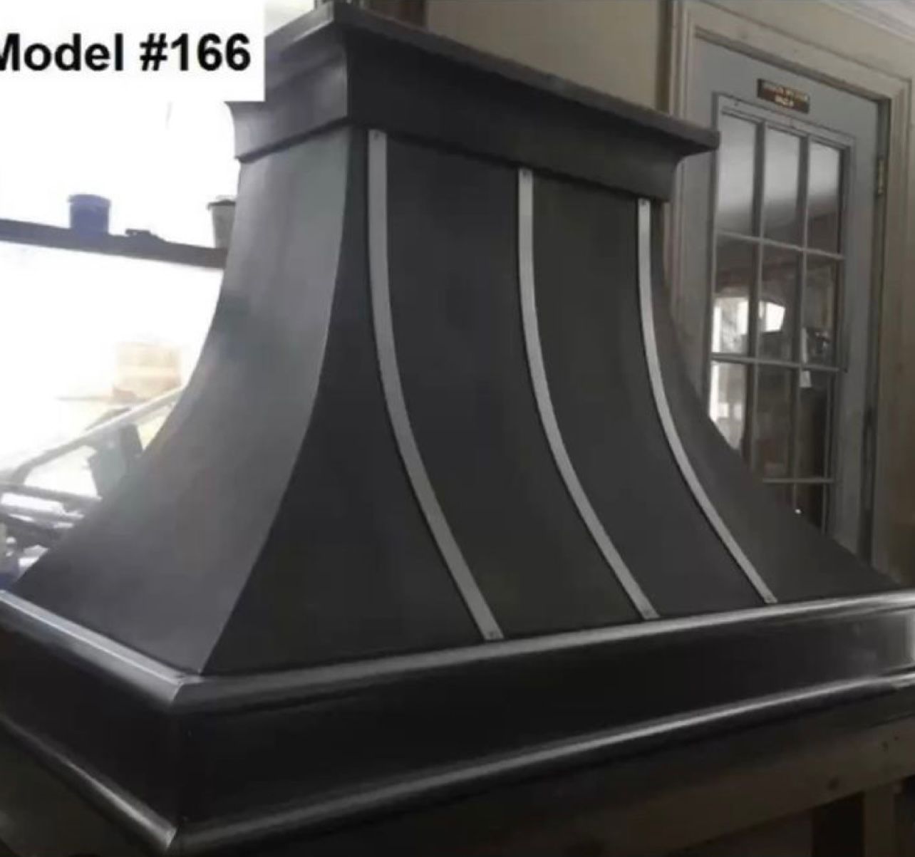 Black range hood with curved silver trim, shown indoors beside a door.