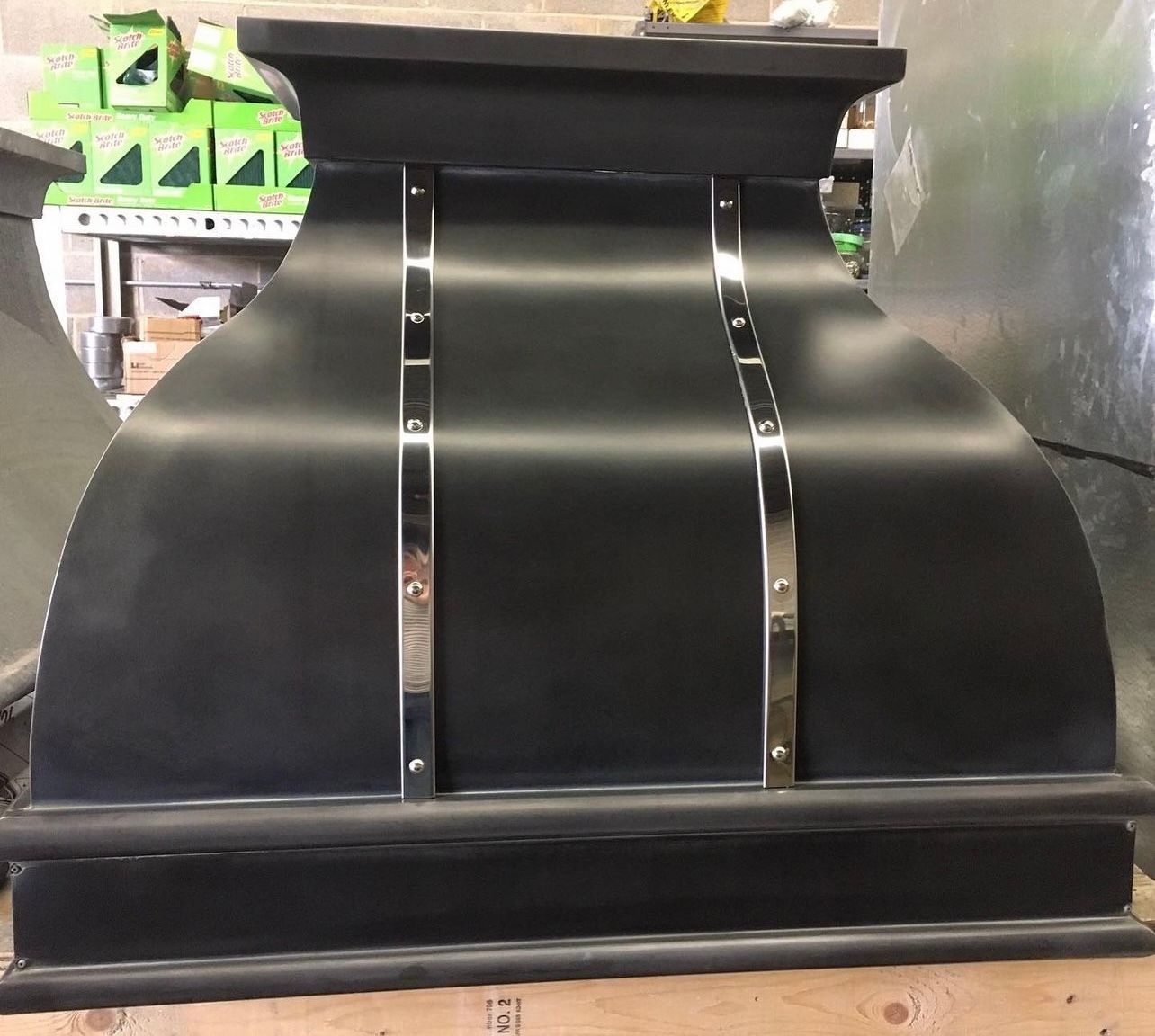 Black curved metal display fixture with vertical silver strips on a warehouse shelf