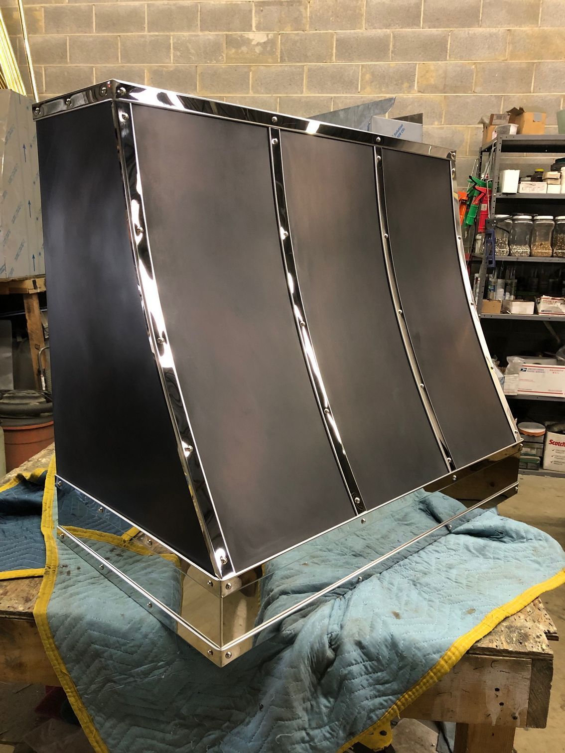 Black curved metal panel assembly on a workbench in a workshop, with taped seams and a towel underneath.