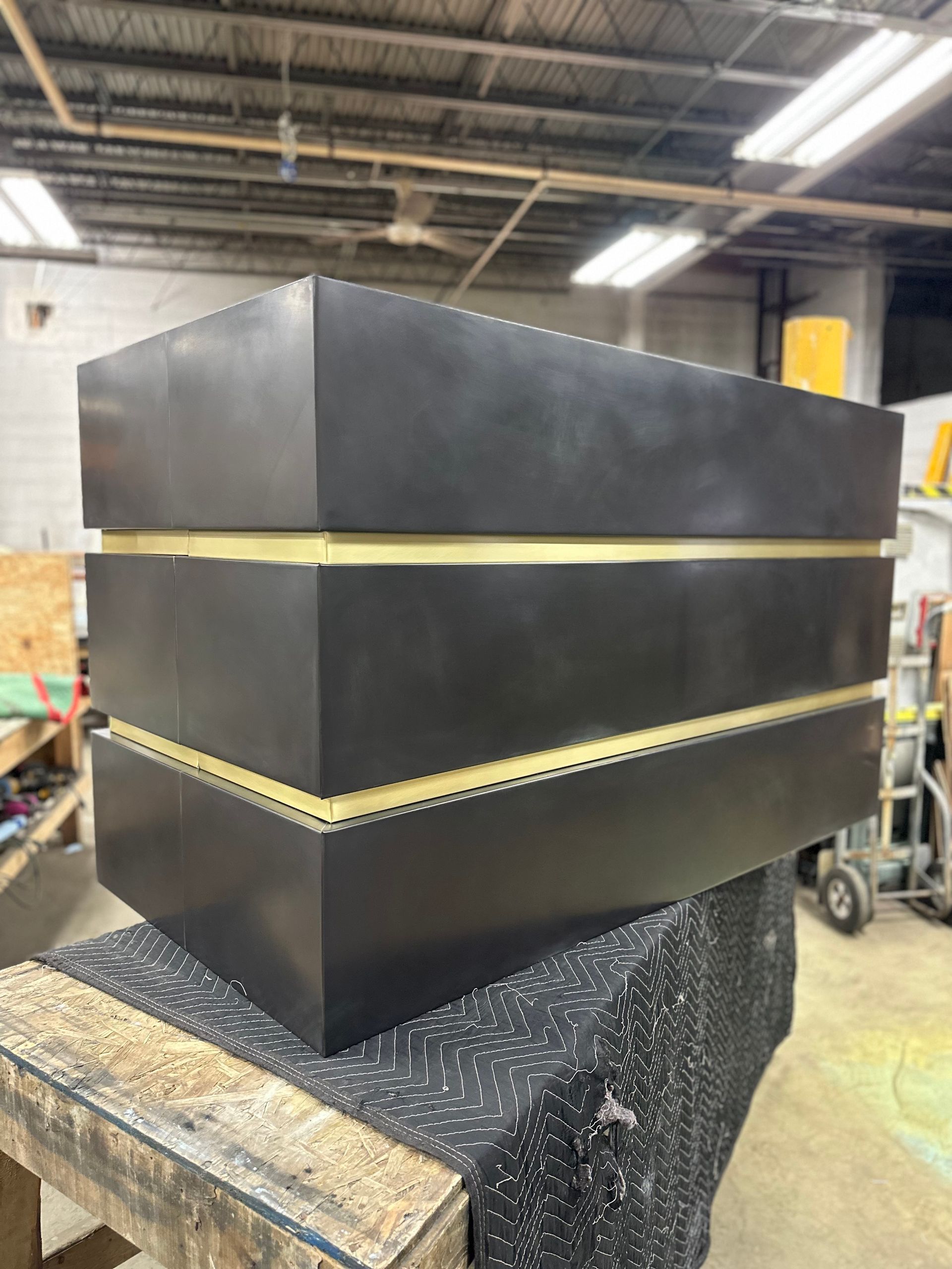 Large black industrial box with gold trim in a workshop, sitting on a covered workbench