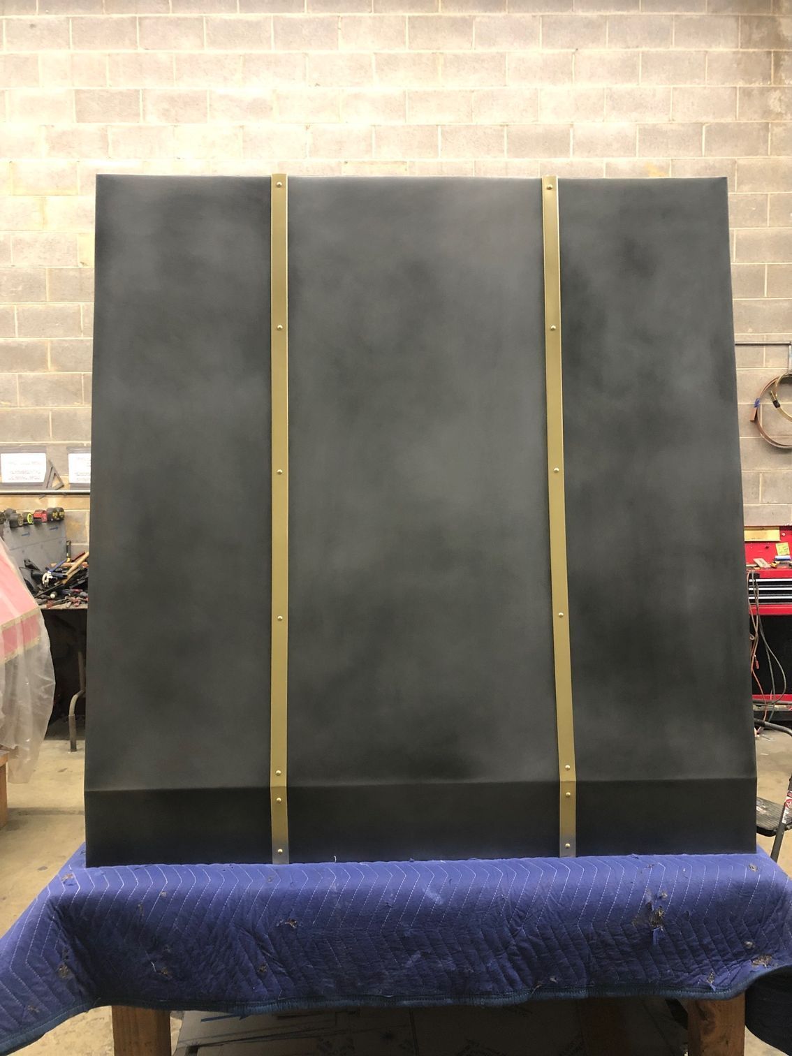Black board with three gold vertical stripes on a blue-covered table in a workshop.