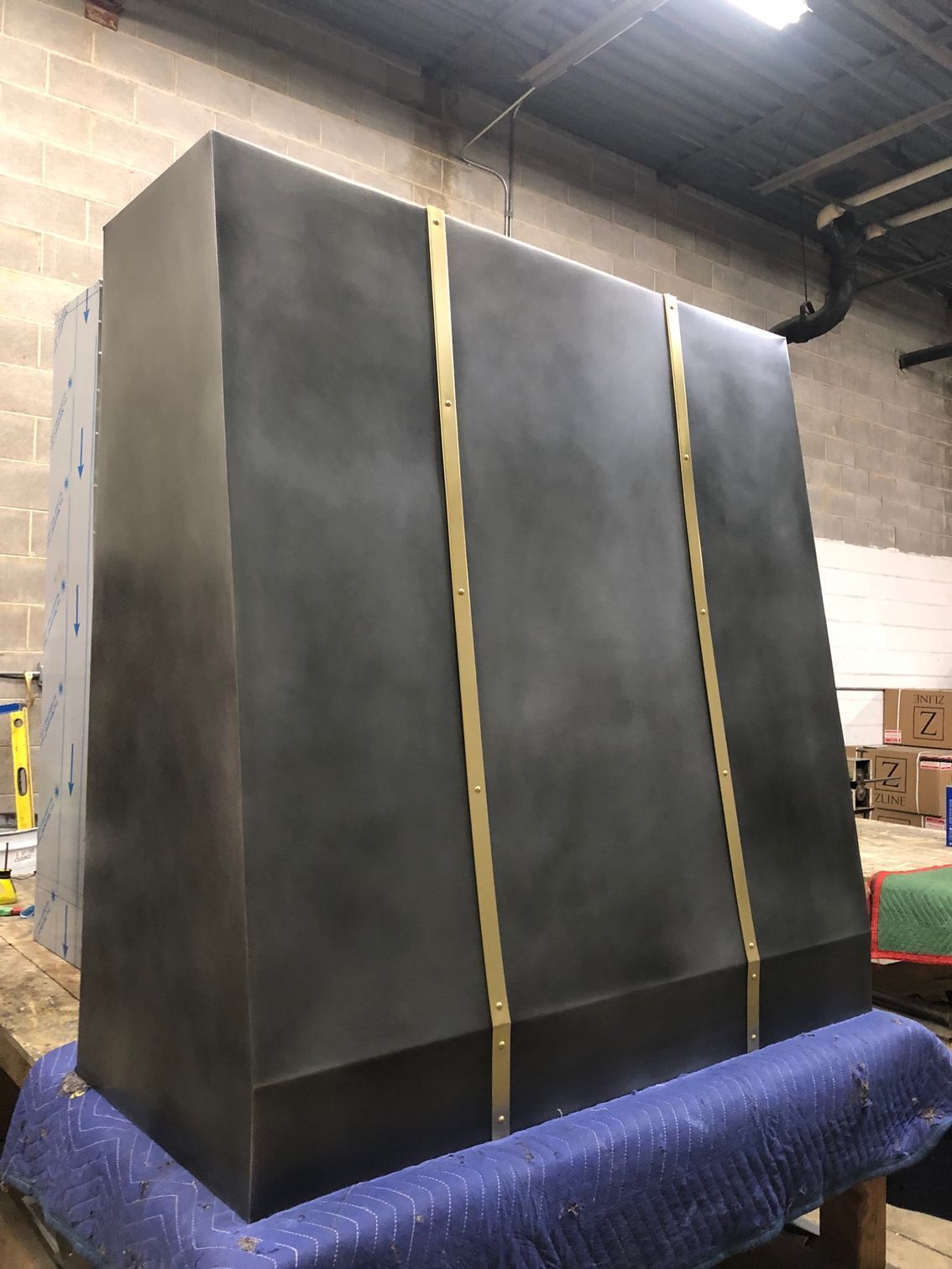 Large black shipping crate wrapped in yellow straps, sitting on a blue pallet in a warehouse