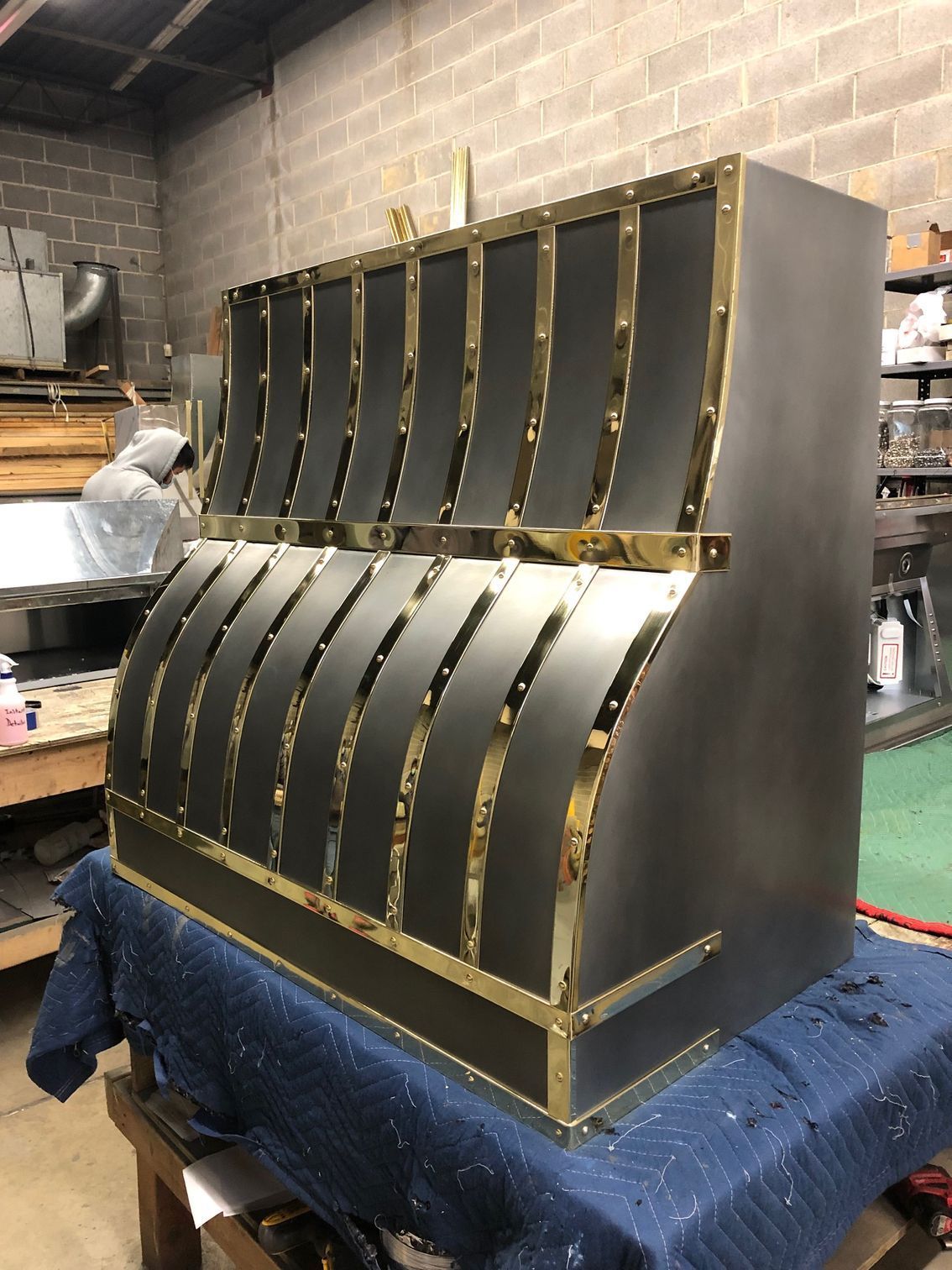 Gold-framed black metal display rack in a workshop, with curved rows and shelves on a blue-covered table