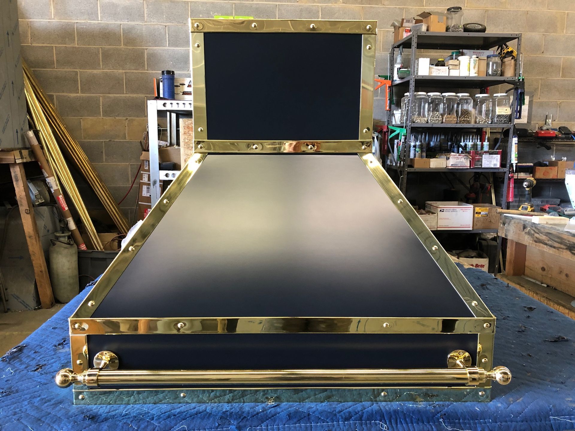 Gold-framed black and gray mechanical device on a workshop floor, with a hinged rectangular panel upright.
