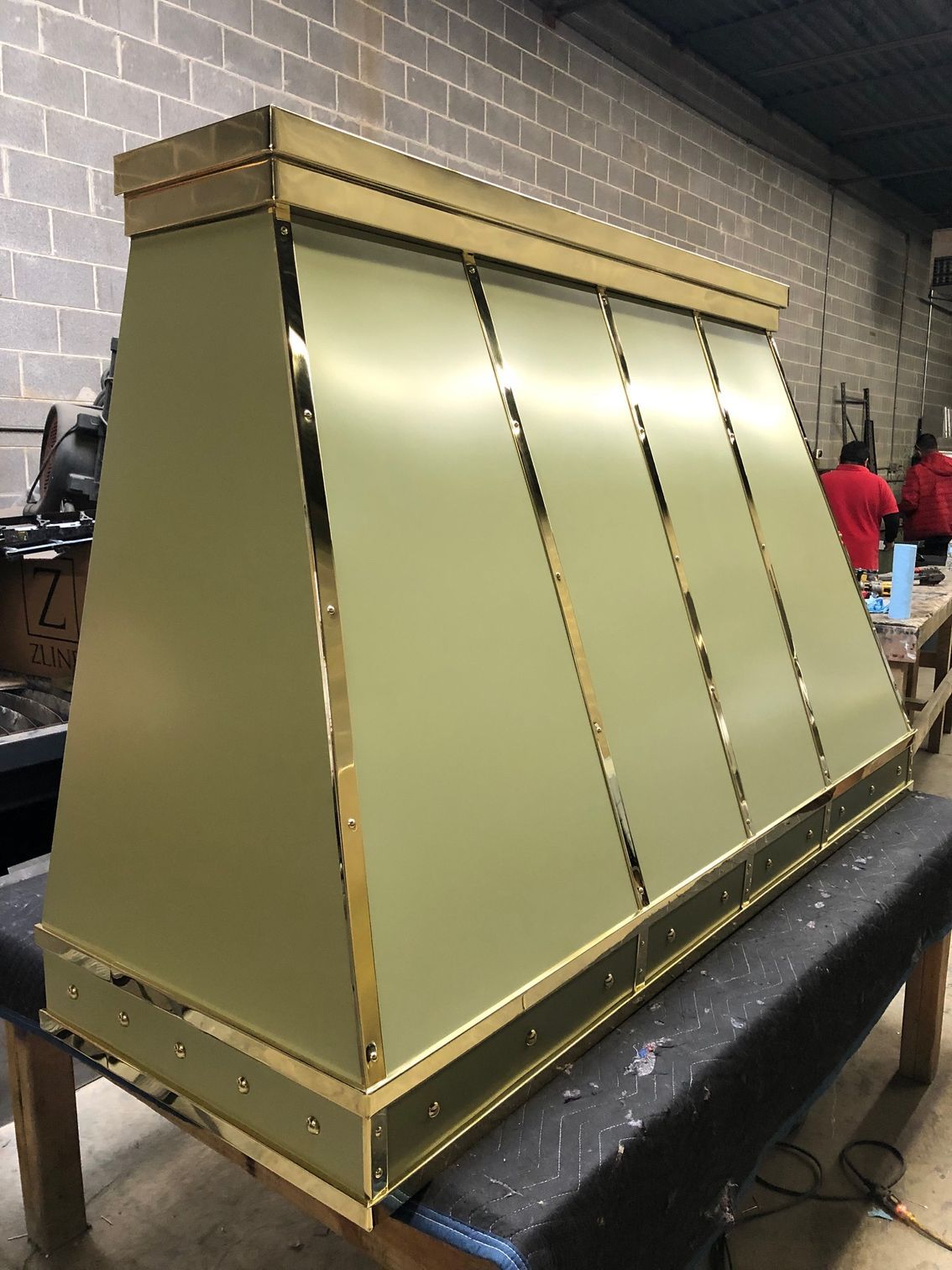 Gold-colored metal hood or enclosure on a black platform in a workshop setting