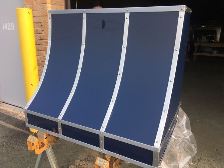 Blue curved metal ramp or barrier panel with white supports, shown on a cart in a warehouse.