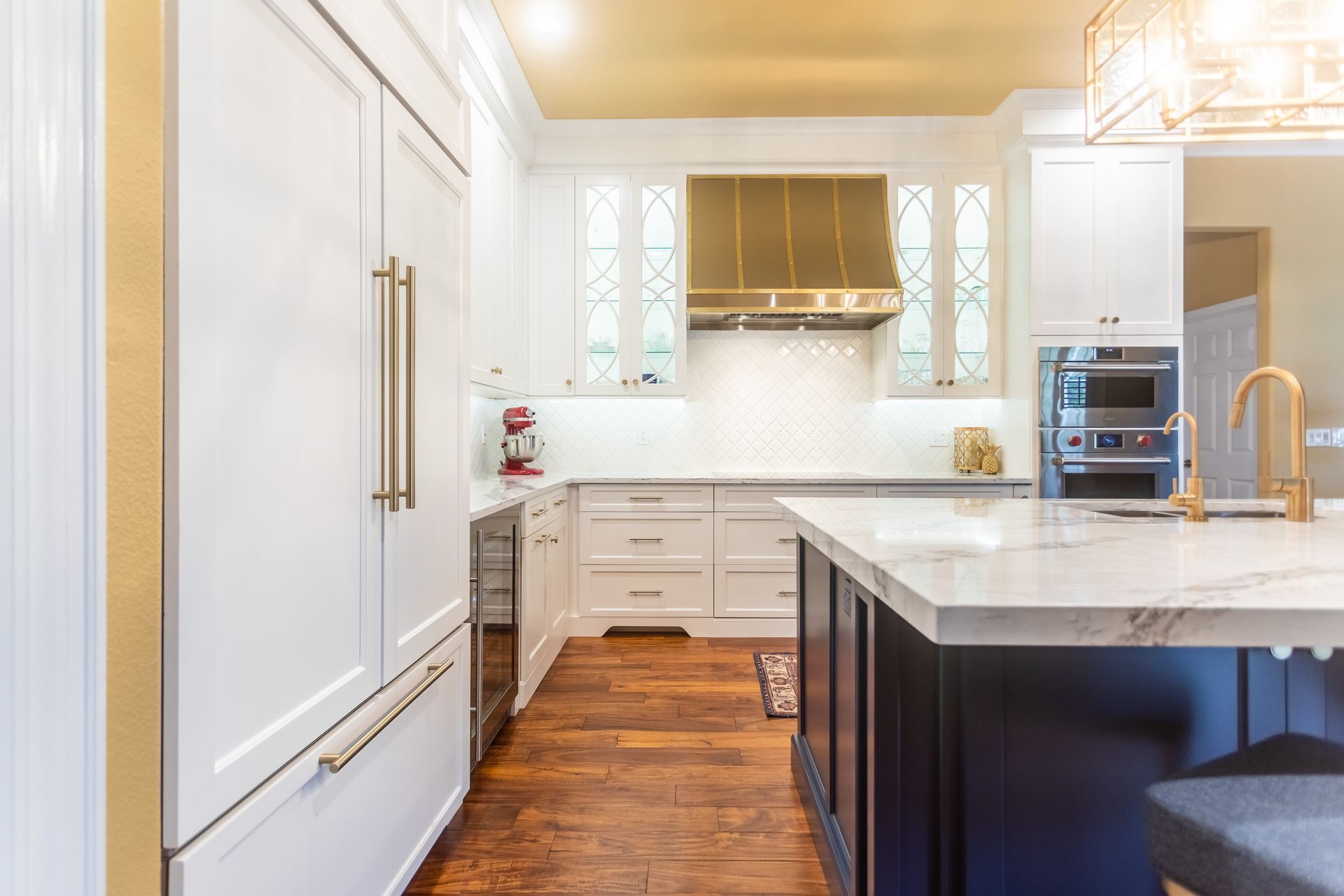 Bright white modern kitchen with marble island, stainless range hood, and hardwood floors