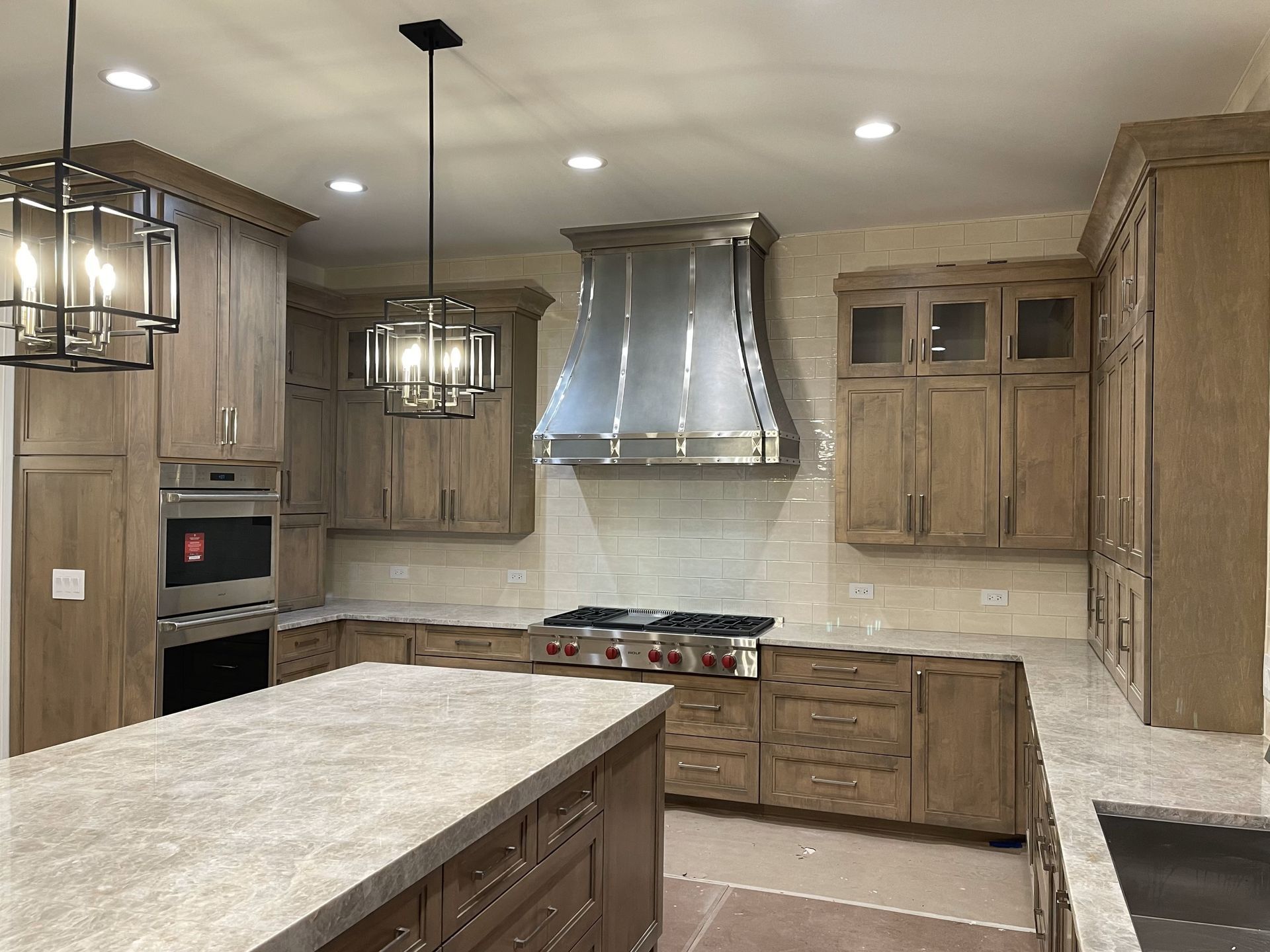 Modern kitchen with wood cabinets, marble island, stainless range hood, and pendant lighting.