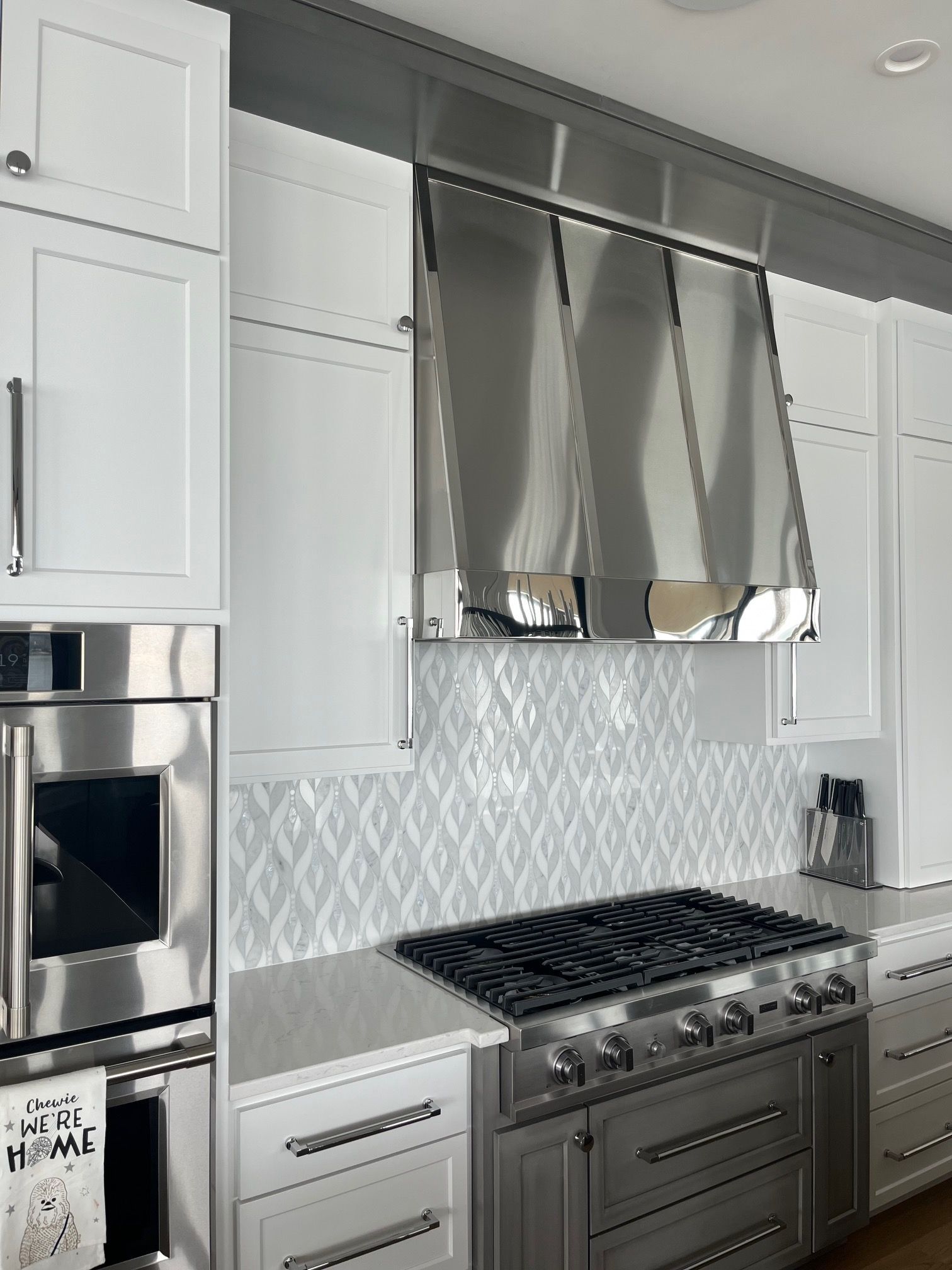 Modern kitchen with white cabinets, stainless steel range hood, and a gas stove with light gray tile backsplash