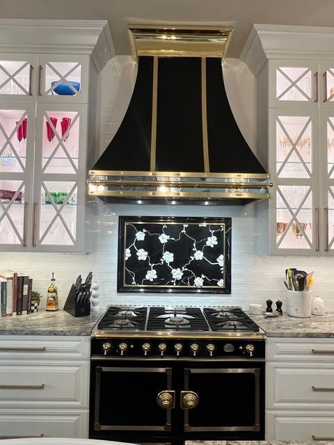 Elegant white kitchen with black stove and hood, patterned backsplash, and glass-front cabinets