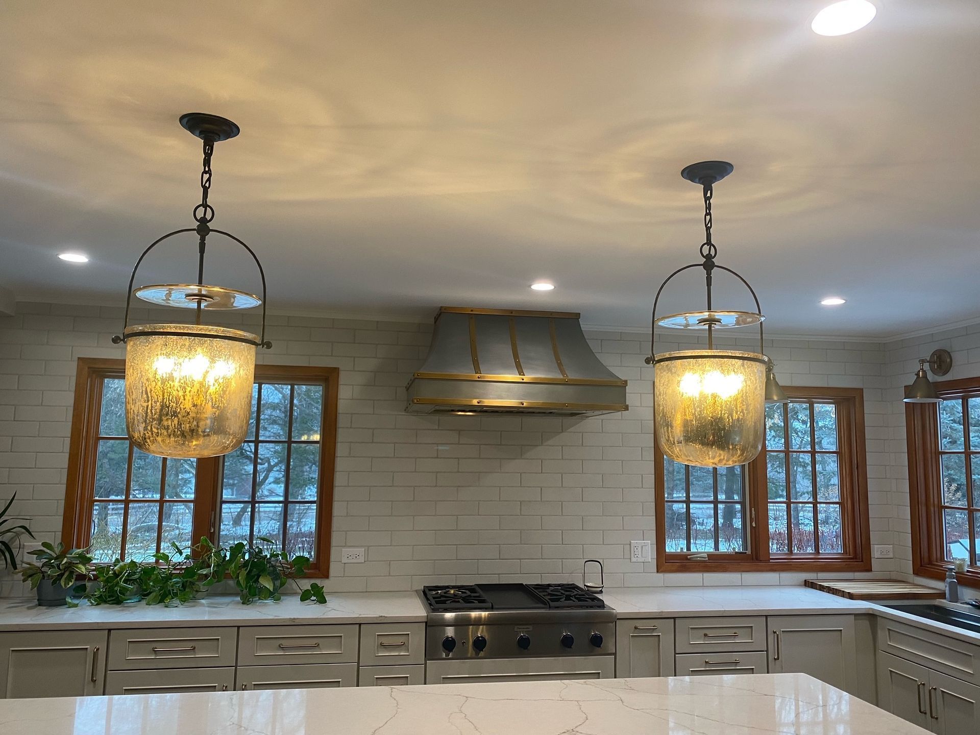 Modern kitchen with white tile backsplash, stainless range hood, gray cabinets, and two pendant lights over the island