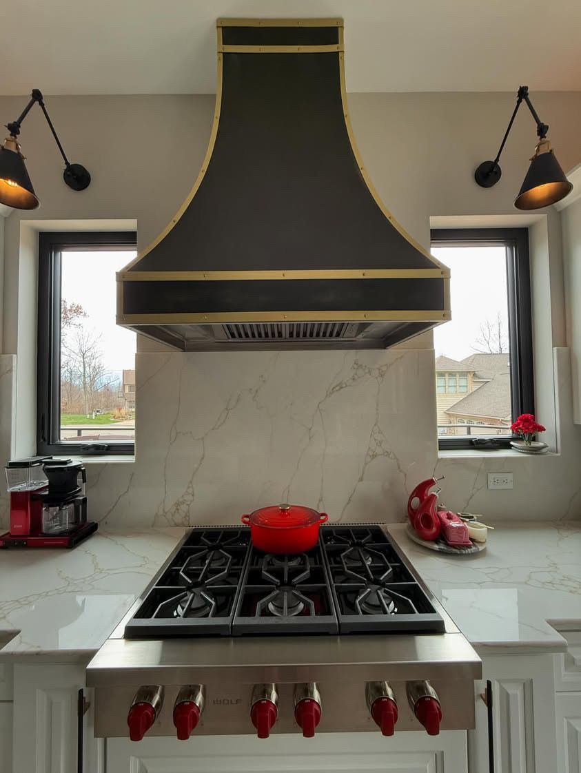 Modern kitchen with black-and-gold range hood, gas stove, red kettle, and red knobs on a white island.