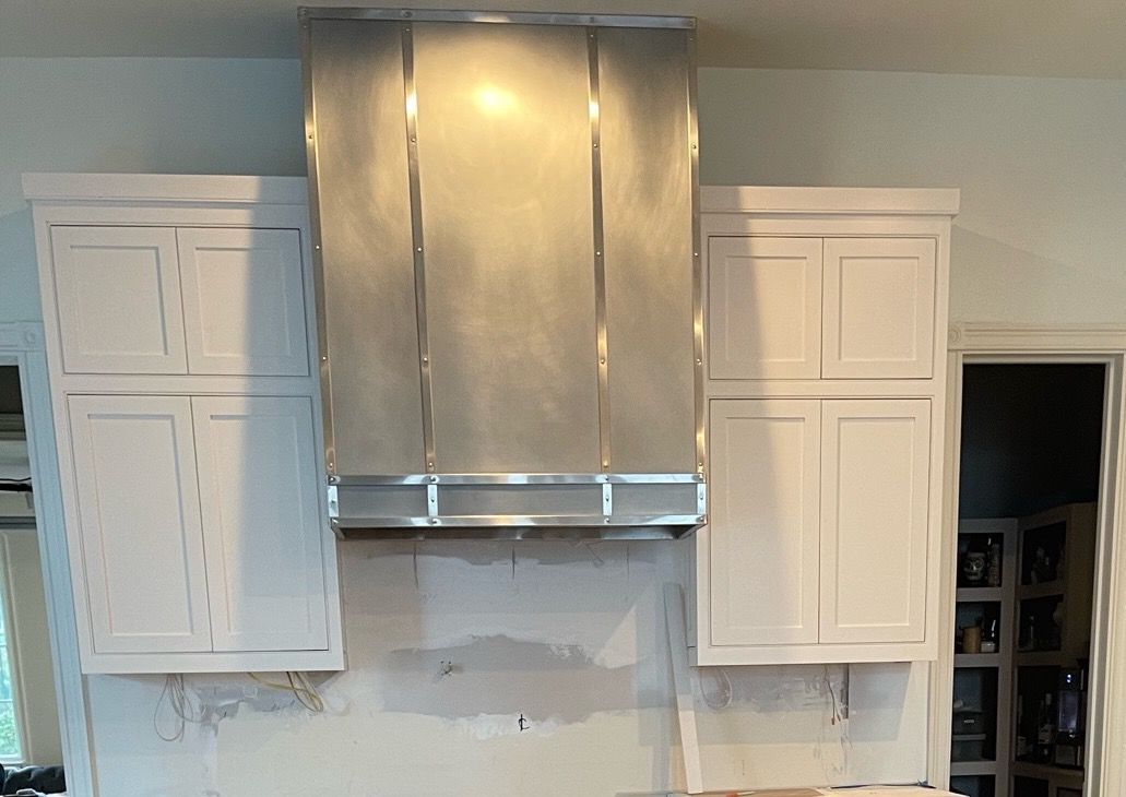 Kitchen wall with three white cabinets flanking a stainless steel range hood, unfinished backsplash below.