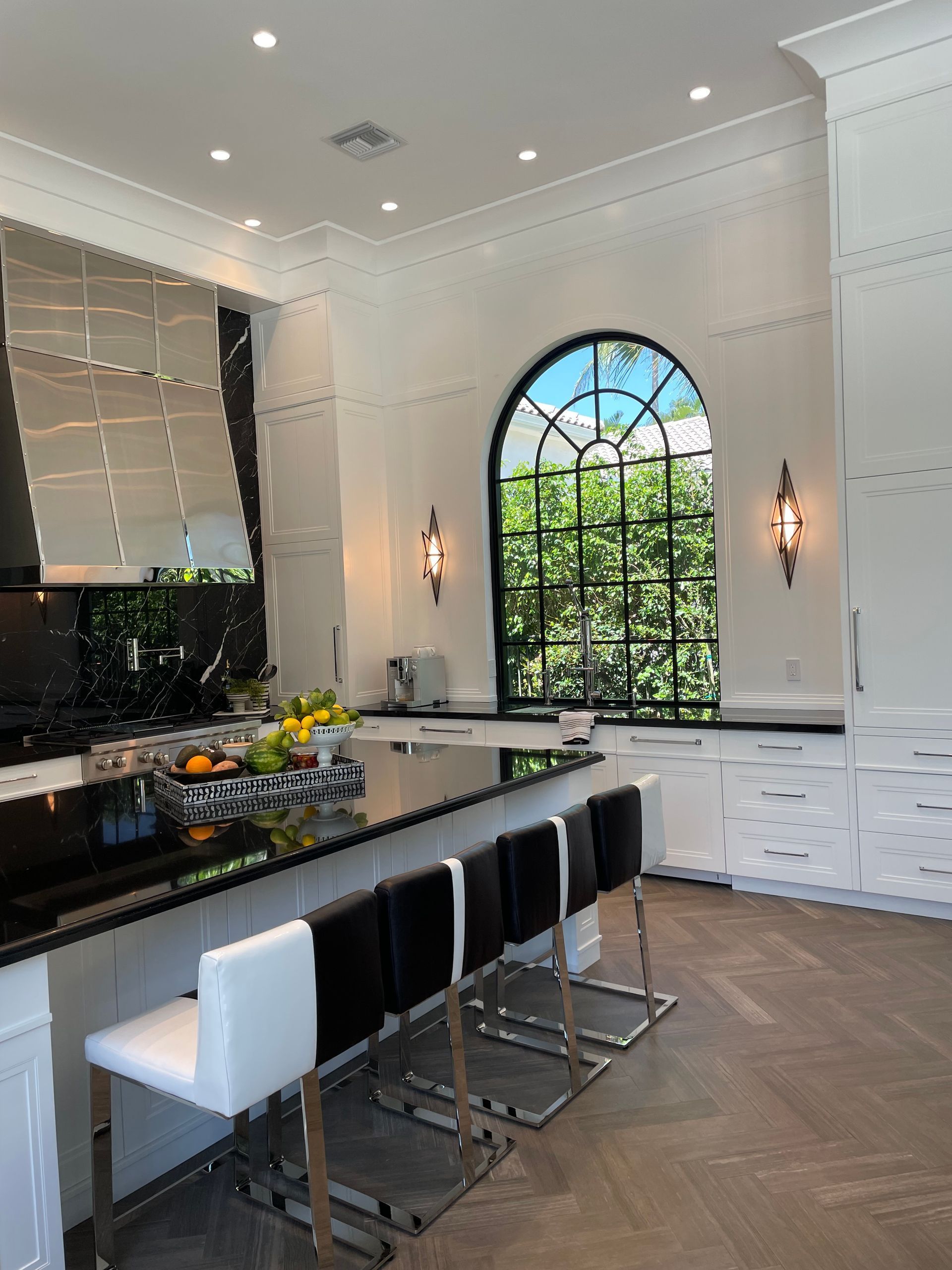 Modern kitchen with black island, white bar stools, arched window, and white cabinets