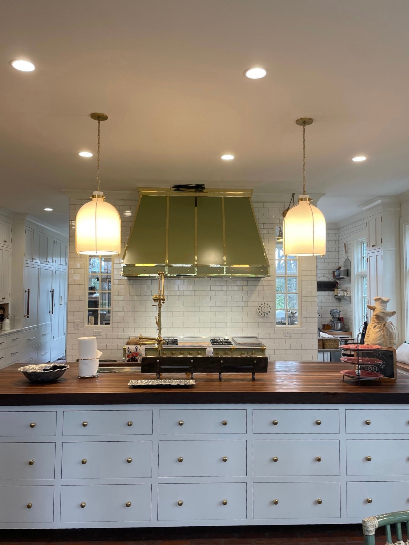 Bright kitchen with white cabinets, wooden island, green range hood, and pendant lights