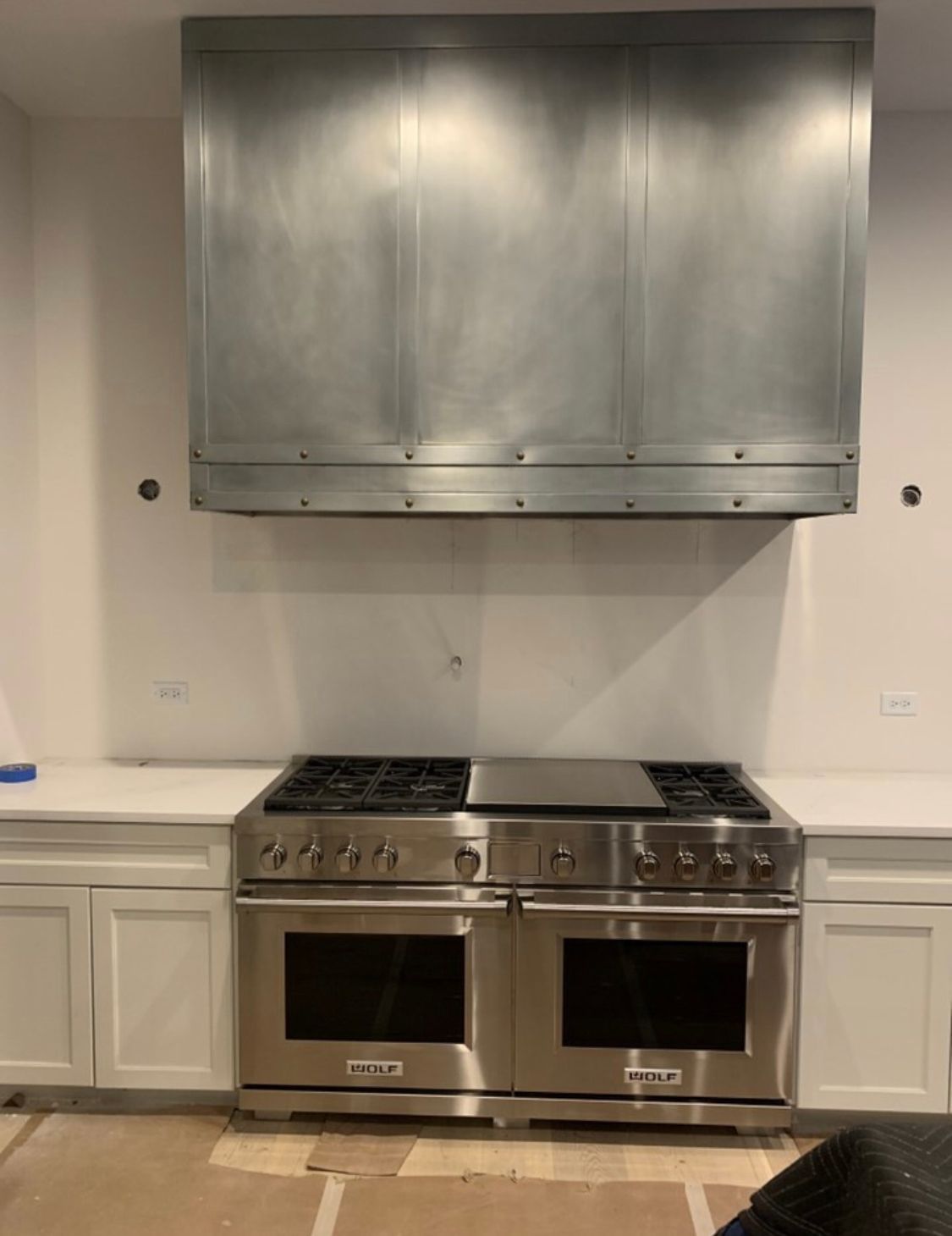 Modern kitchen with stainless steel range and hood, white cabinets, and a light-colored backsplash.