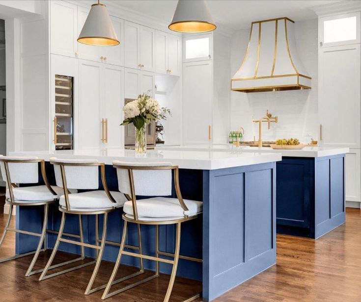 Bright white kitchen with blue island, brass accents, and four stools