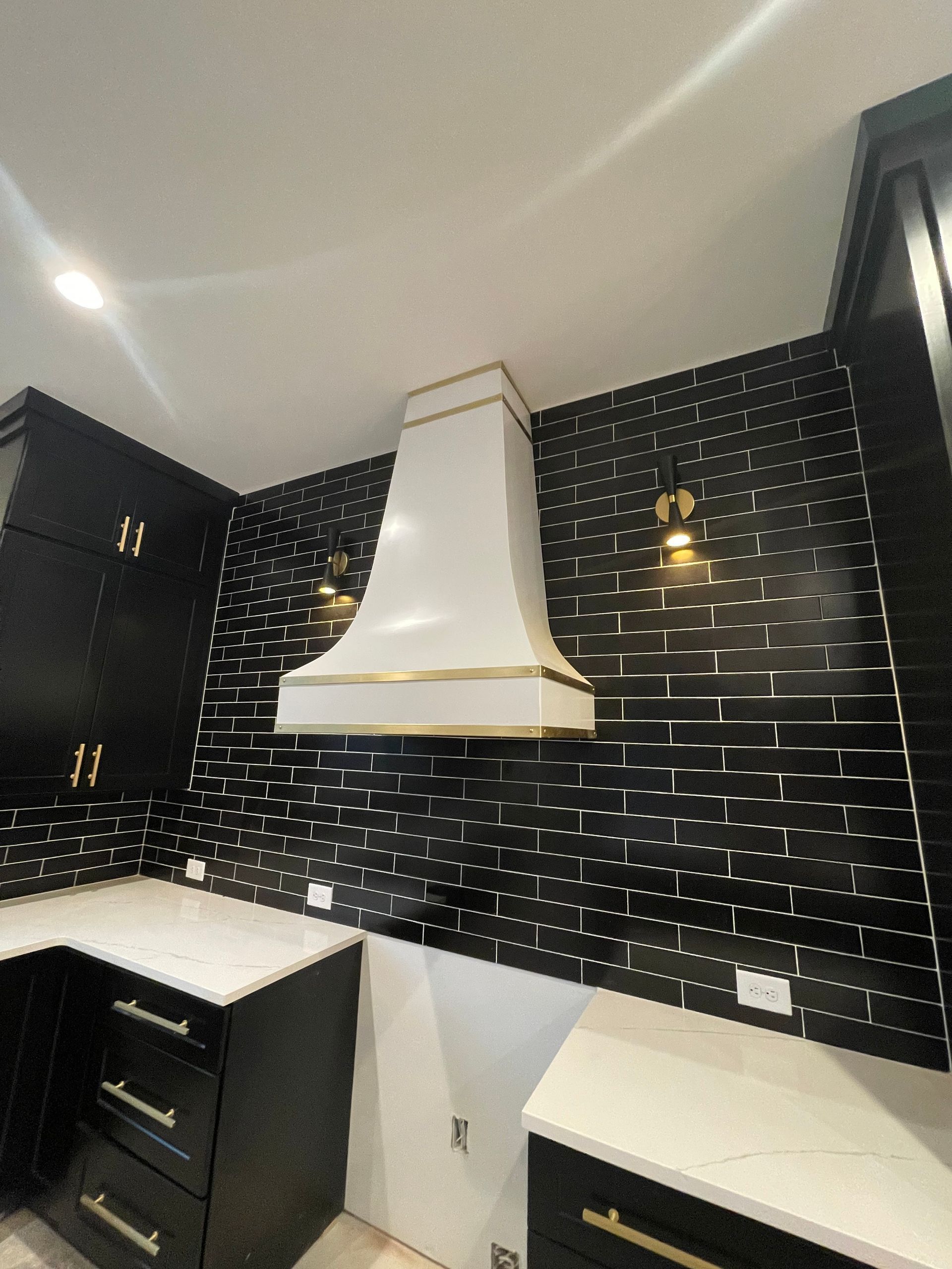 Black-and-white kitchen with glossy tile backsplash, white range hood, and dark cabinets and counters