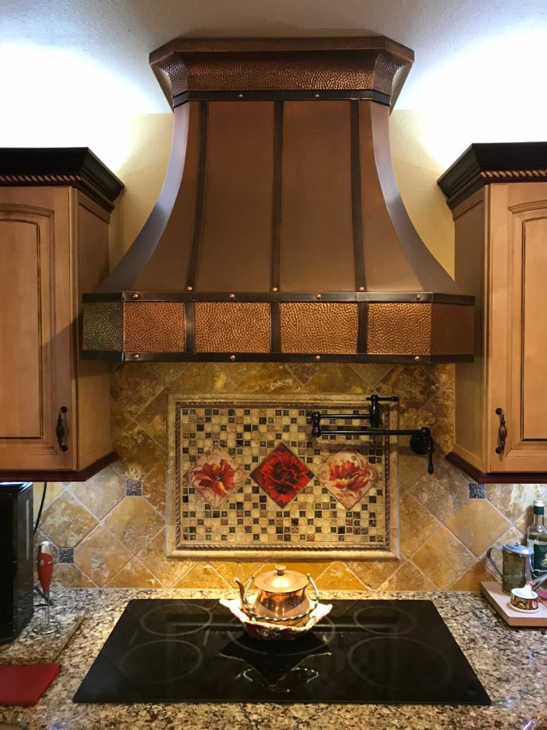 Kitchen range with copper hood, mosaic backsplash, and black stovetop, with a teapot on the burner