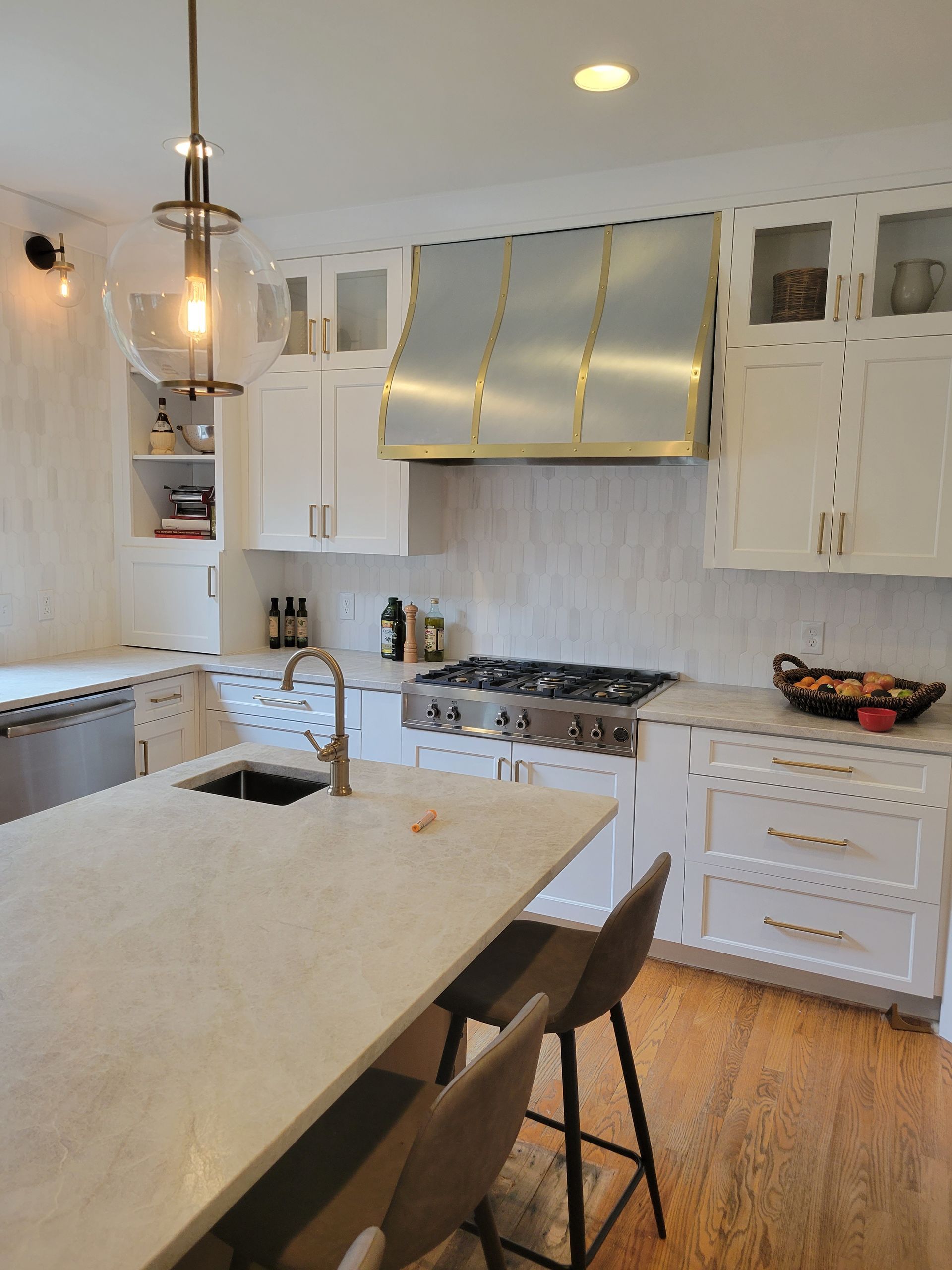 Bright modern kitchen with island, white cabinets, stainless range hood, and hanging pendant lights