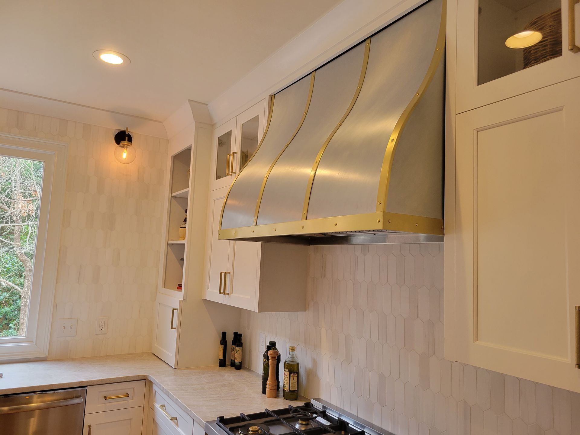 Modern kitchen with white cabinets, gold-trimmed range hood, and light wood backsplash tiles