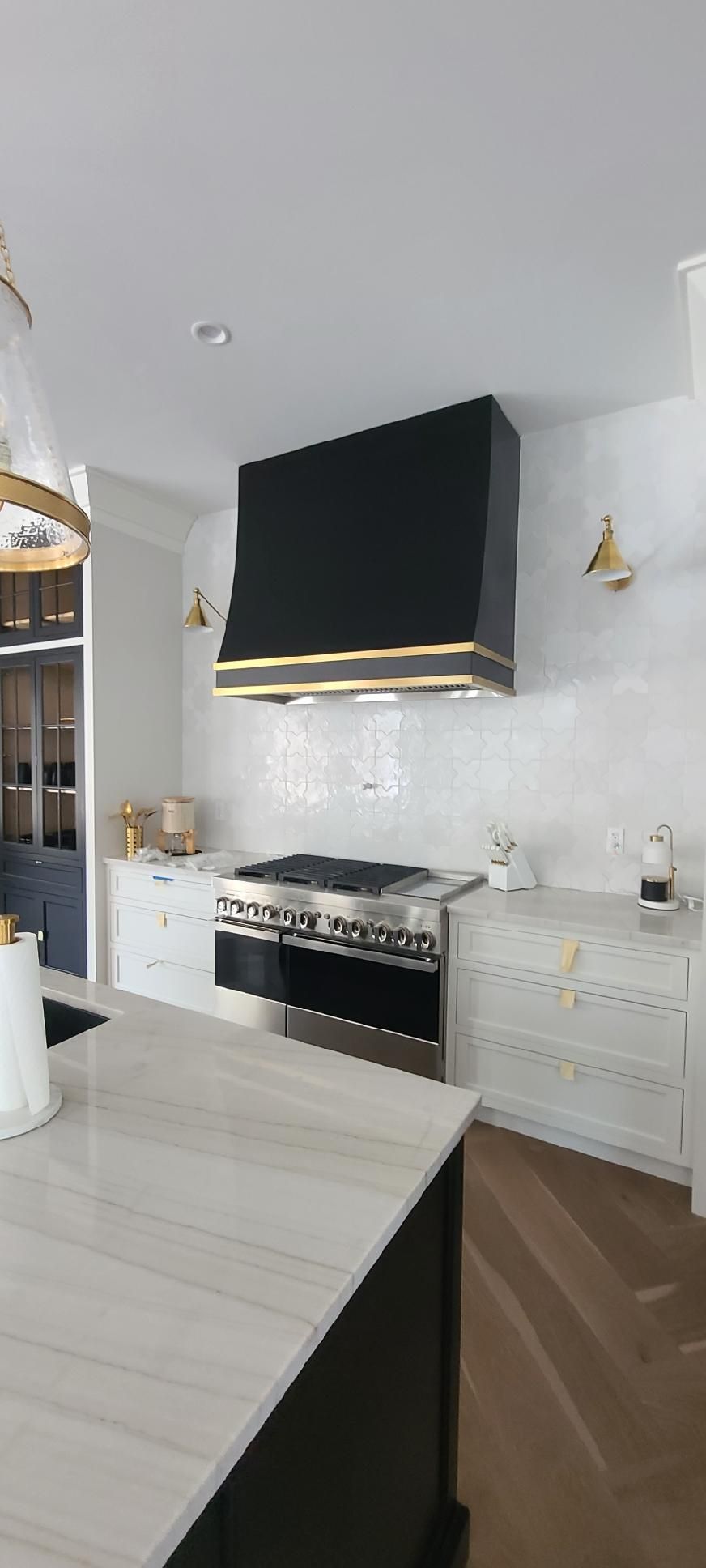 Modern white kitchen with black range hood, marble backsplash, and dark wood floors