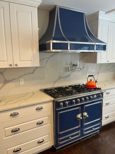 Blue range and hood in a bright white kitchen with marble backsplash and dark wood floor